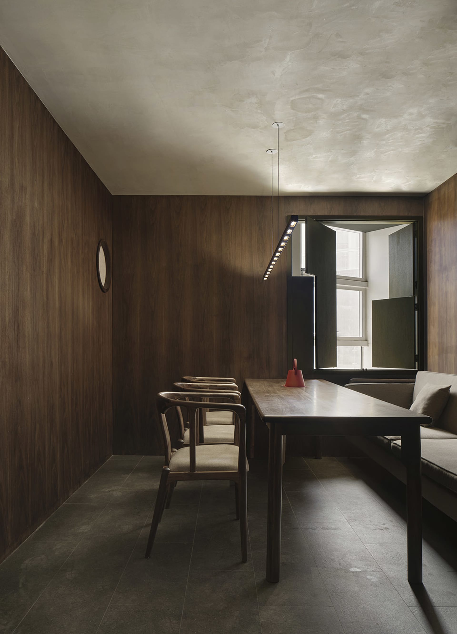 Cozy living area with a dining table, couch, and wooden walls, featuring a modern design and a clock on the wall