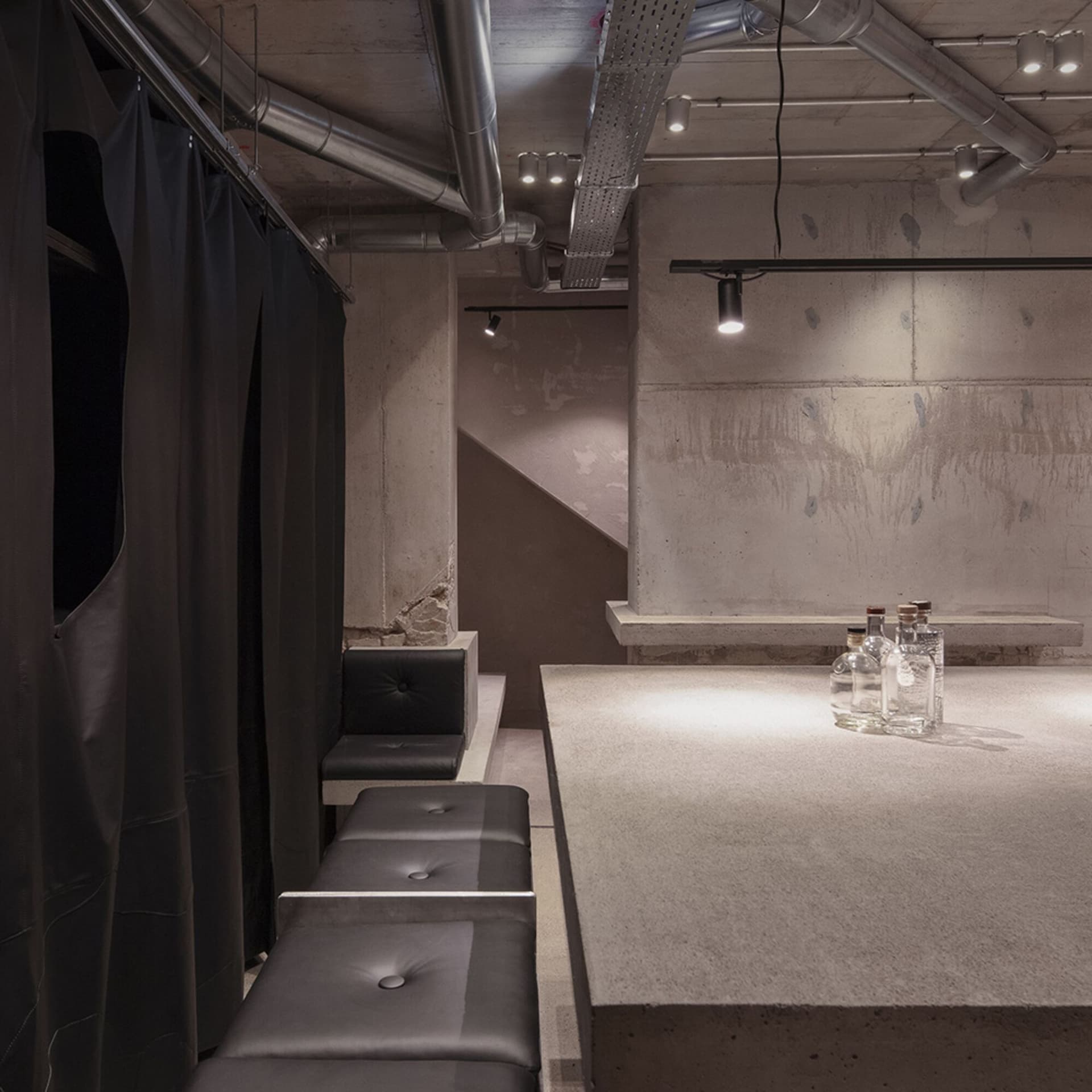 Modern bar space with a concrete countertop, stone wall, and black leather chairs, featuring bottles on display