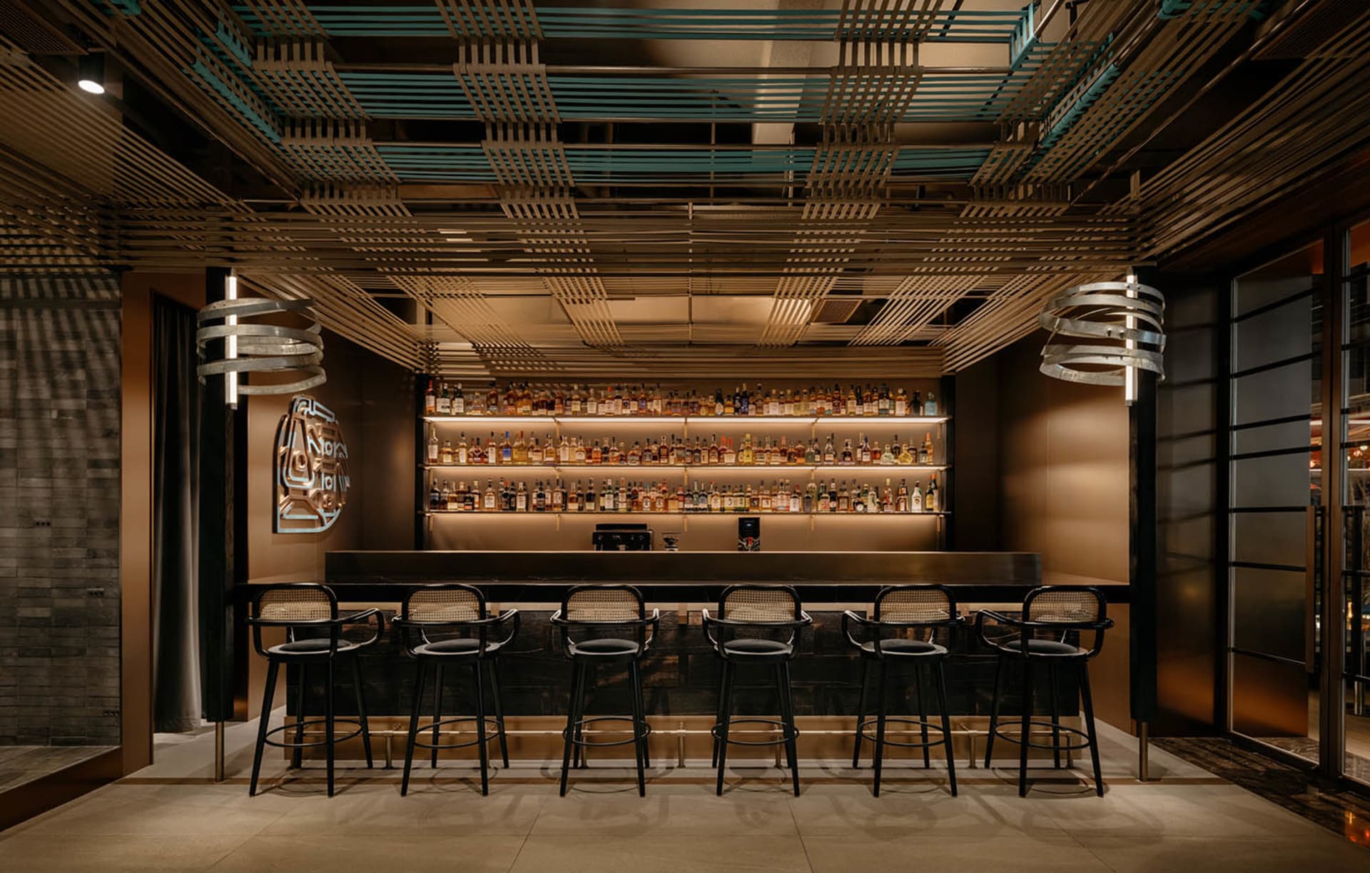 A modern bar with a long counter and stools, featuring bottles and a stylish design