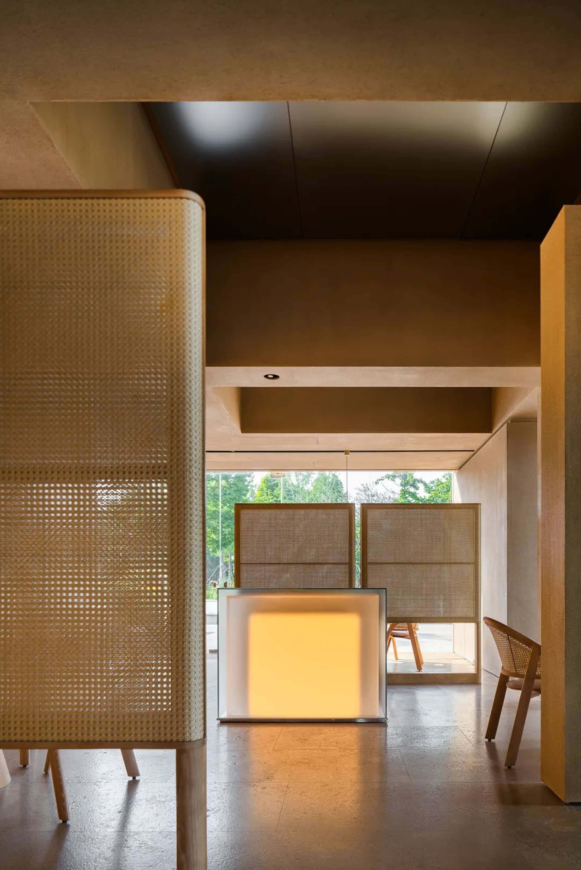 A warm and inviting living space with a glass wall separating two rooms, featuring a wooden table and comfortable seating arrangement, with natural light streaming through the glass wall