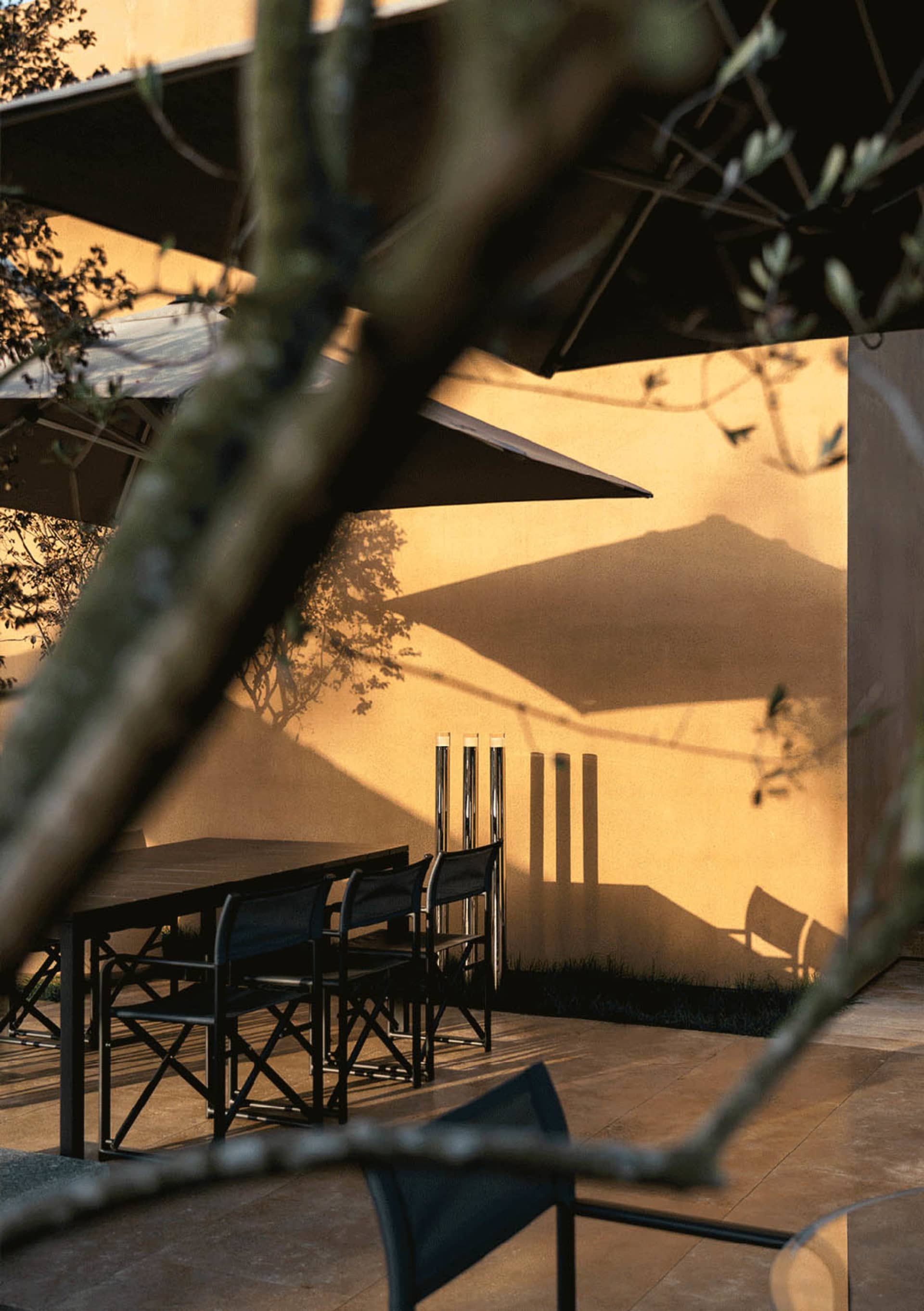 A wooden table surrounded by black metal chairs under an umbrella in a relaxed outdoor dining area