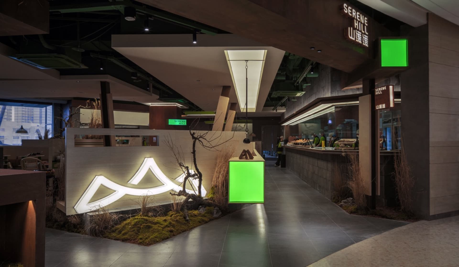 A lively cafe with a large green display box, people standing and sitting throughout the space, and a mix of industrial and decorative elements