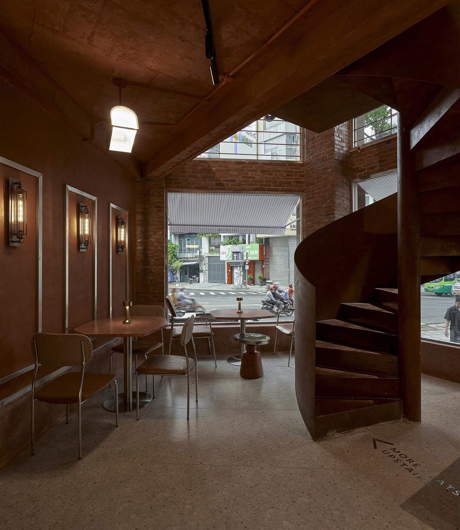 A modern cafe with a spiral staircase, brown and red tones, and cozy lighting from table lamps