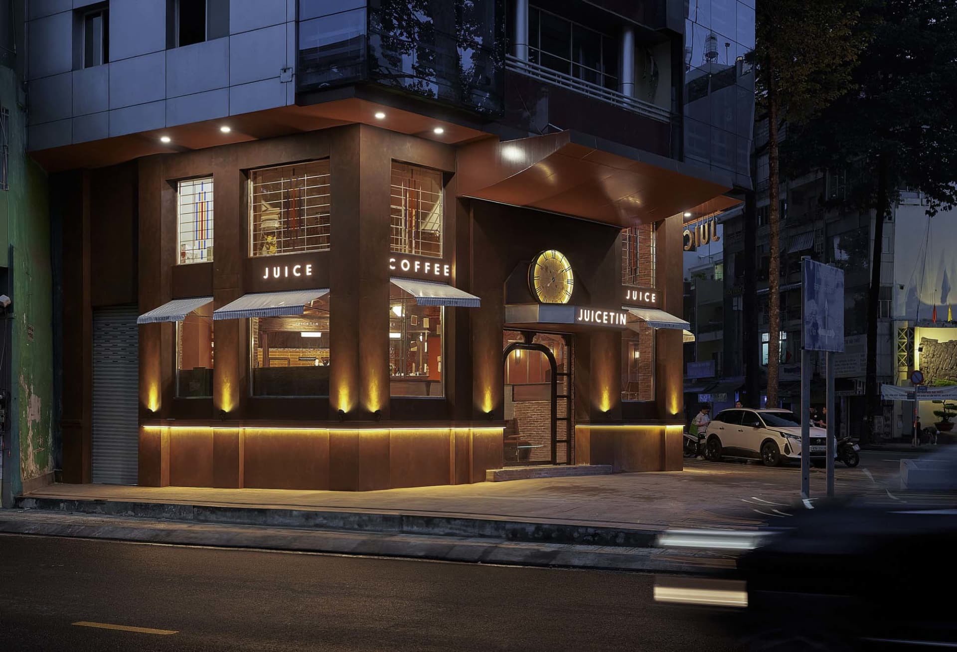 Exterior view of a cozy coffee shop at night with a brown building, large window, umbrellas, and parked cars
