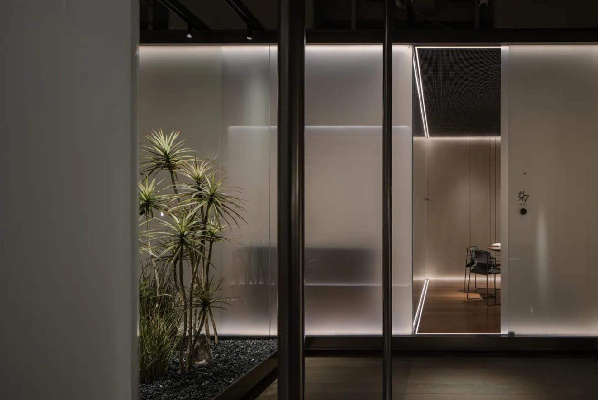 A modern office space with a glass door, two chairs, and a potted plant, featuring a well-lit and comfortable atmosphere