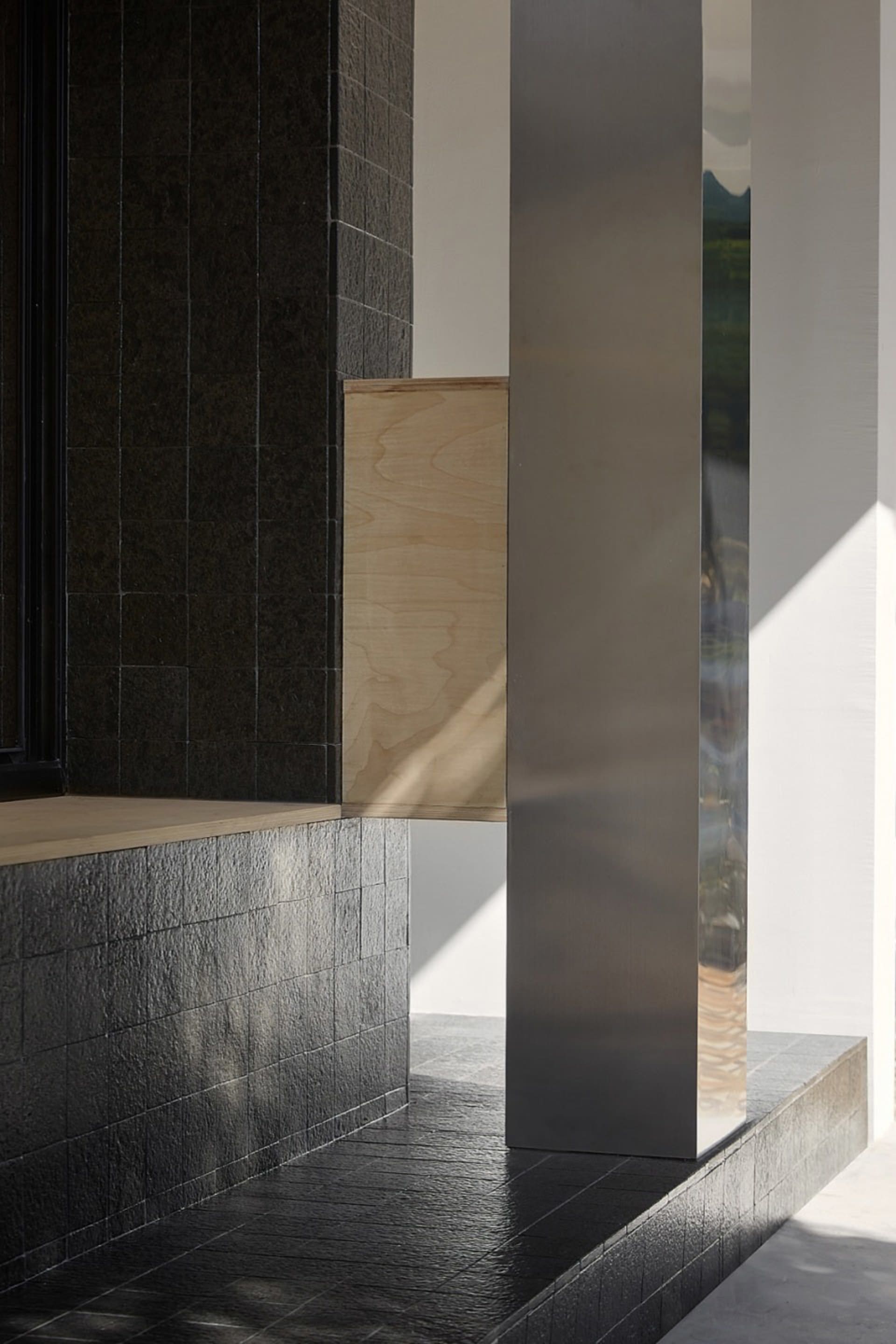 Black building with a wooden wall and a glass wall, featuring three pillars and a window allowing natural light to enter the space