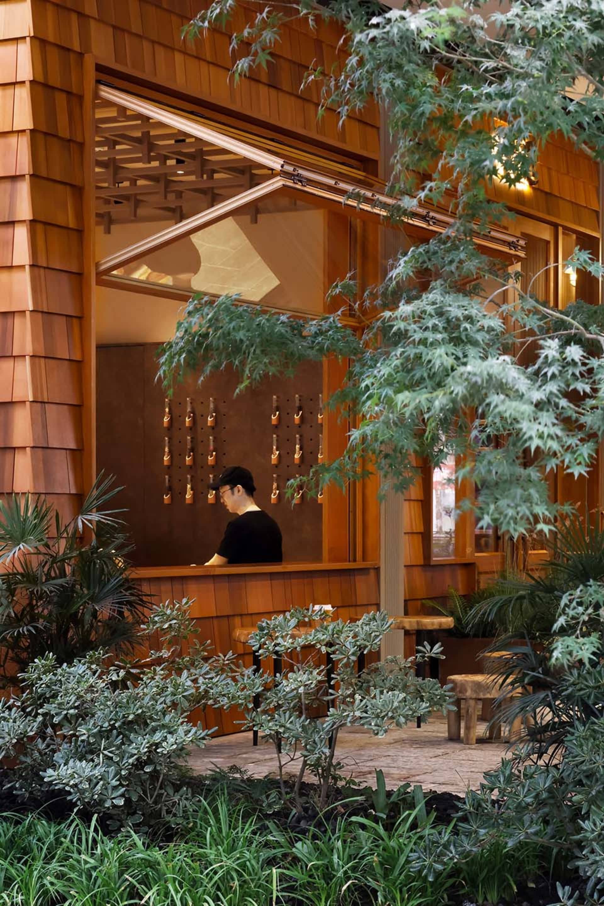 A warm and inviting Asian restaurant with wooden walls, potted plants, and a man working behind the counter