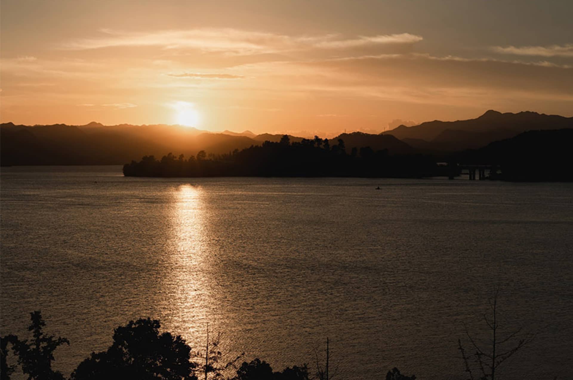 A serene lake scene at sunset with mountains in the background, warm hues of orange and pink in the sky, and two boats on the water