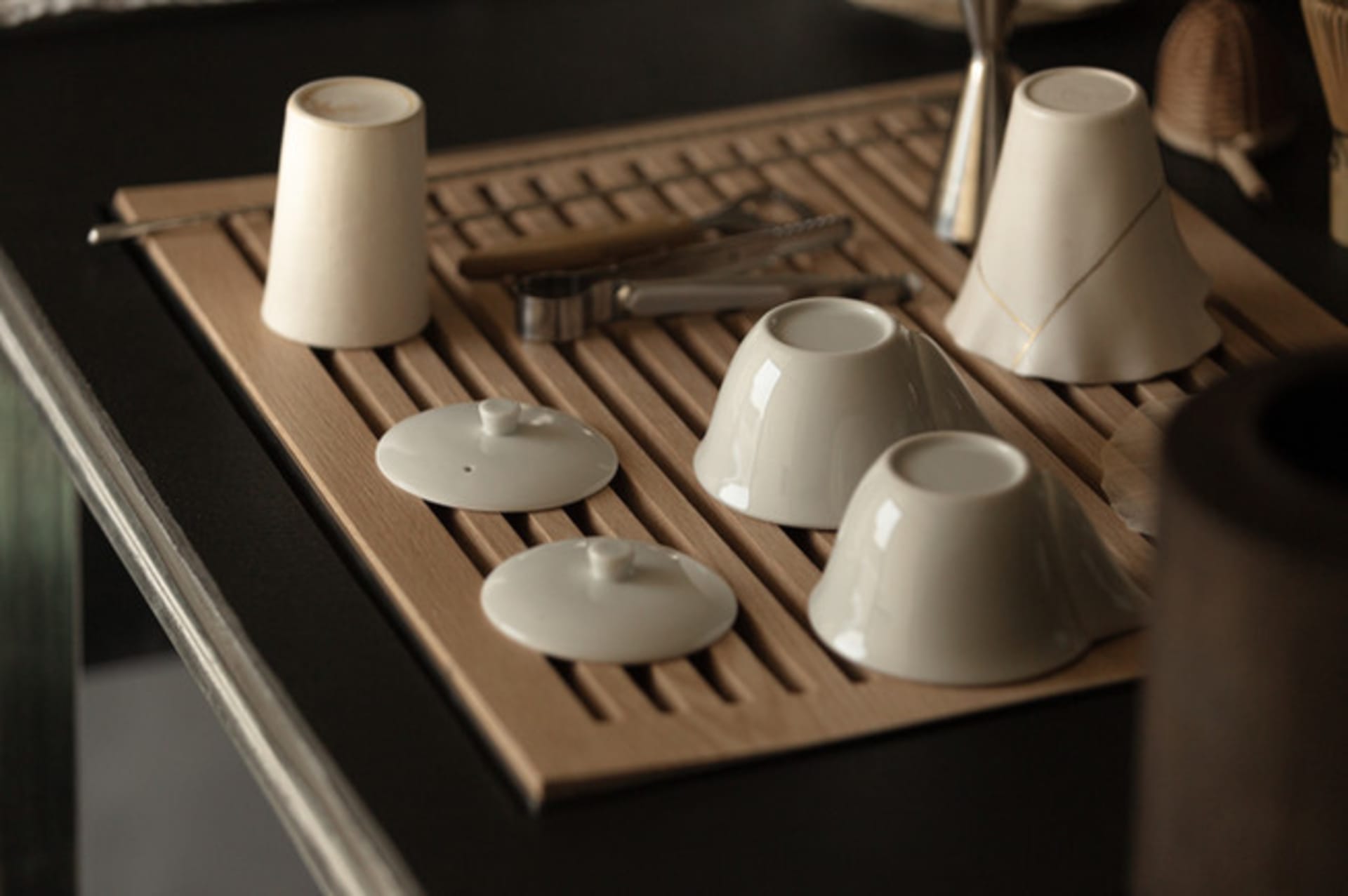 A wooden tray on a table with four cups and two spoons arranged neatly for a meal setting