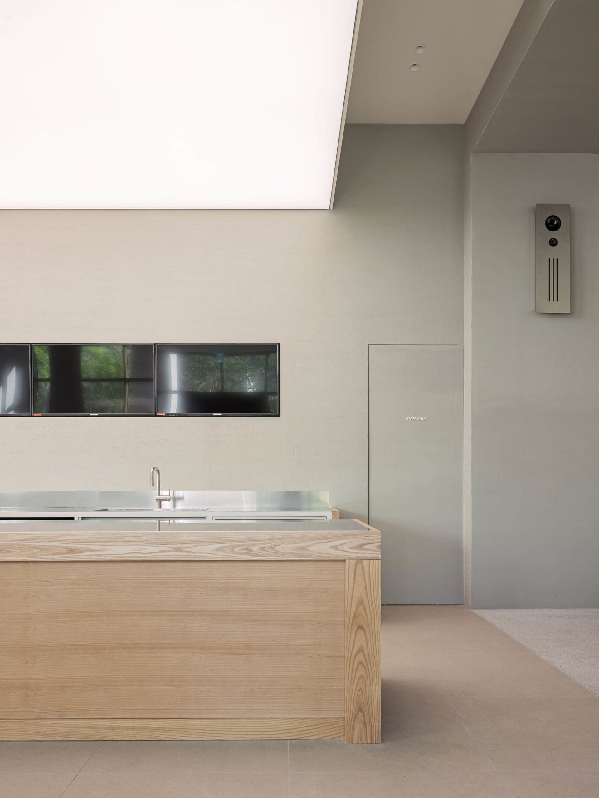 Empty kitchen with a wooden finish, a sink, and a large flat screen TV mounted on the wall, with two remotes nearby