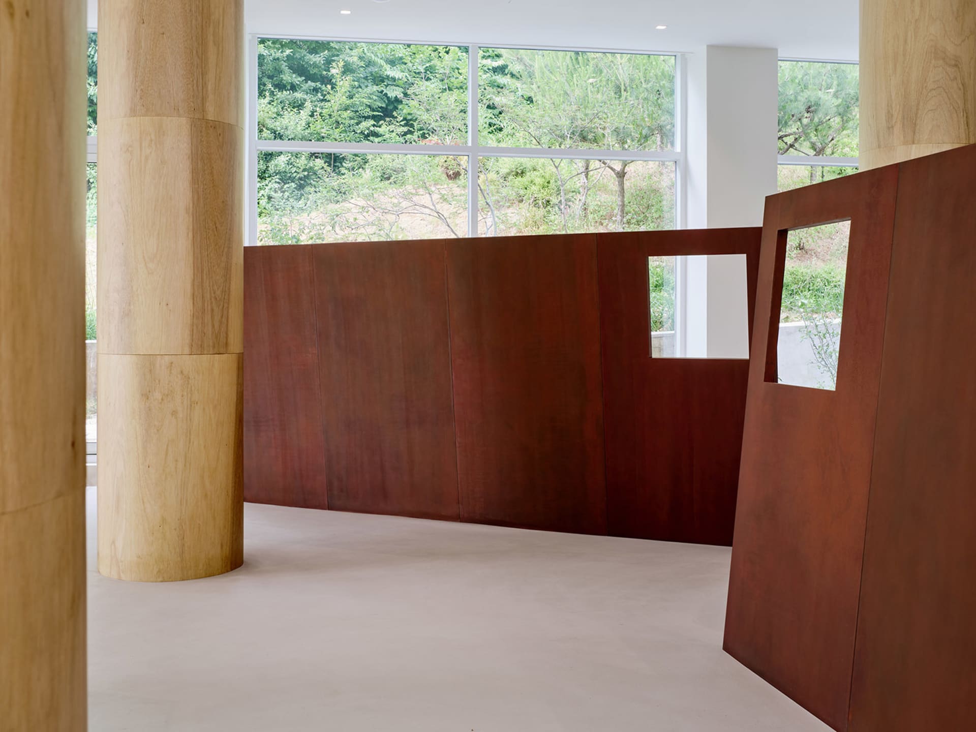 A warm and inviting interior space with a large wooden wall, a red wall in front of a window, and a brown wall, well lit with natural sunlight