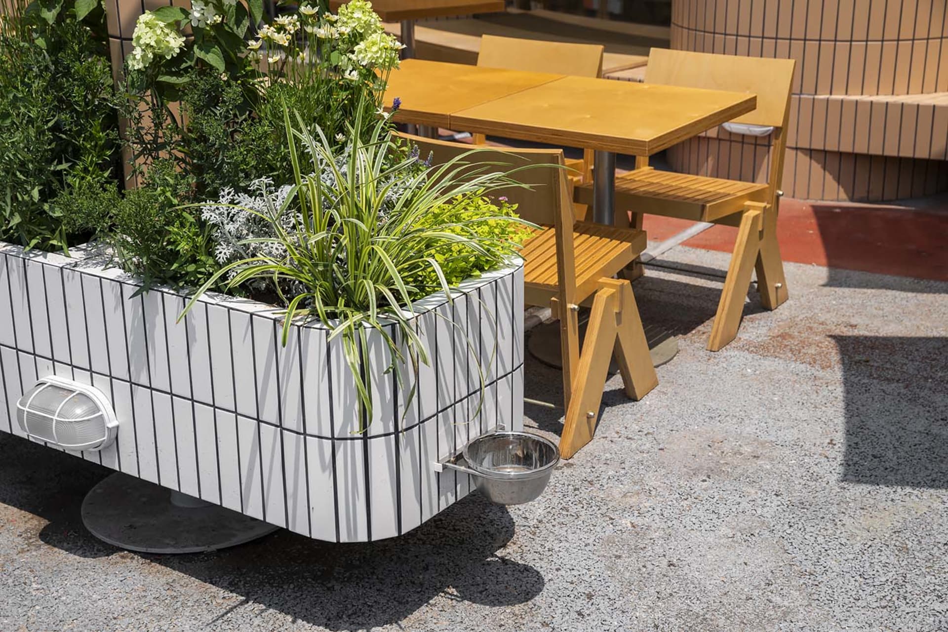 Outdoor dining area with two tables and chairs, surrounded by a potted plant and natural surroundings