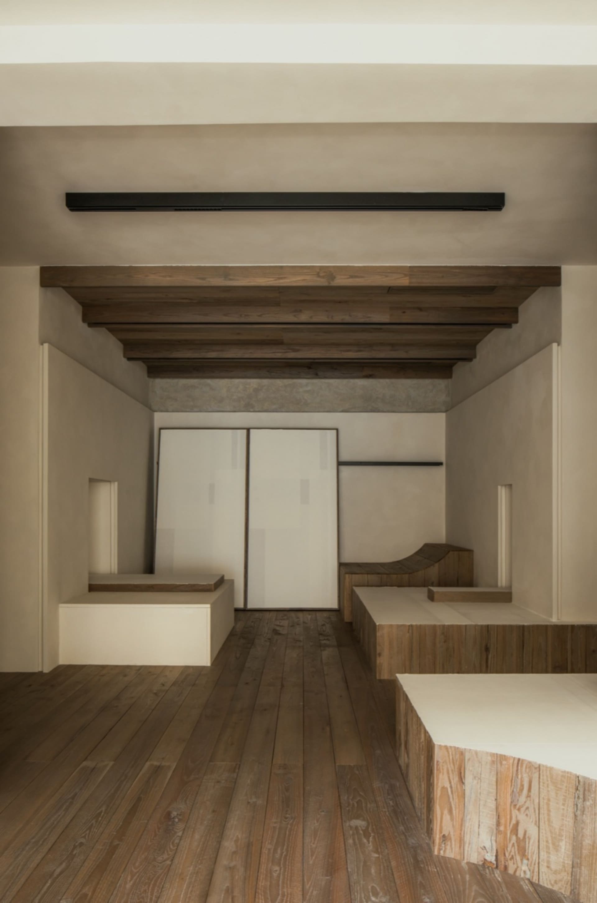 Empty room with wooden floors and walls, featuring two benches and a chair, creating a calm and inviting atmosphere