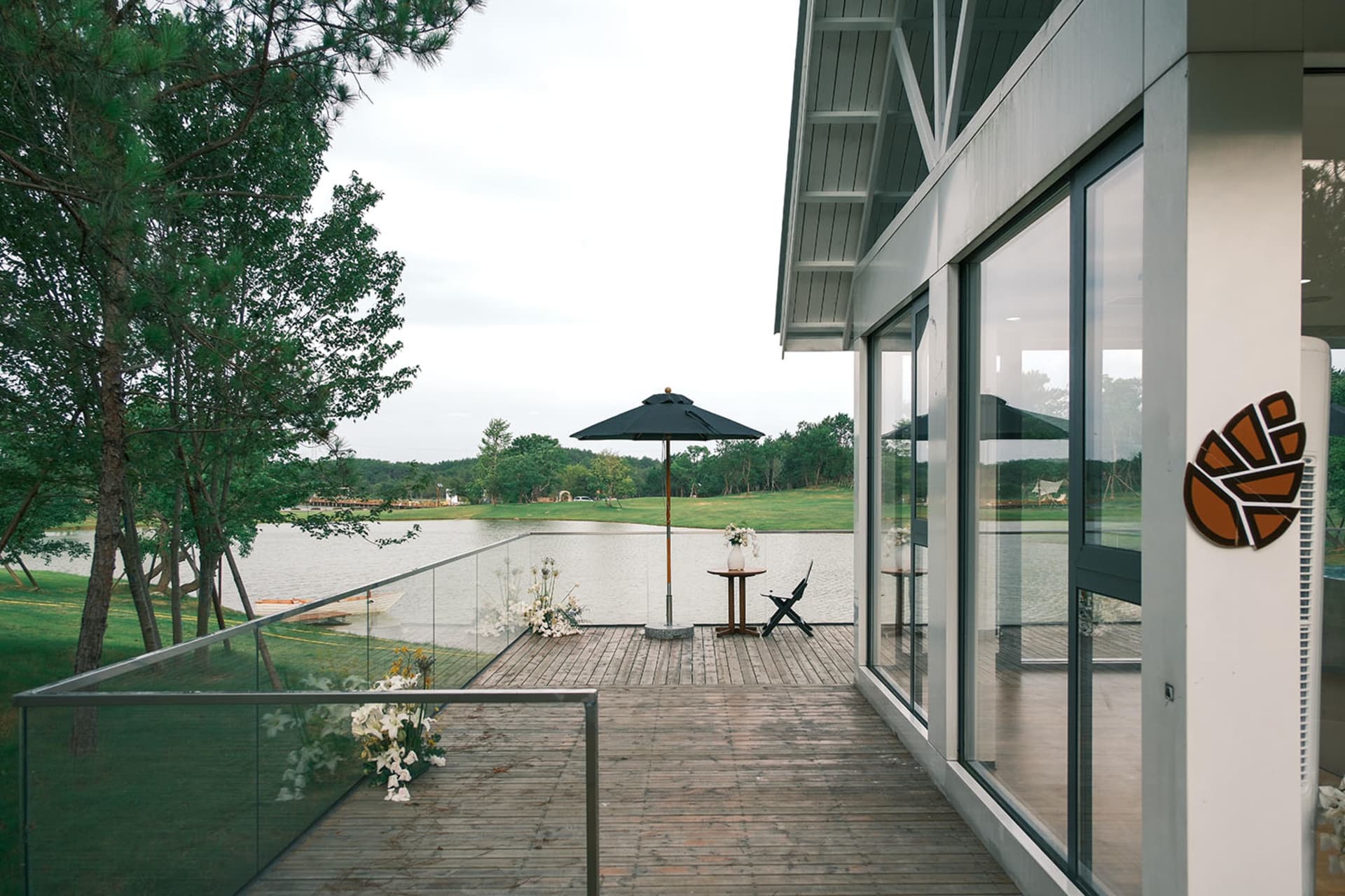 A serene outdoor dining space with a deck overlooking a lake, surrounded by potted plants and comfortable seating