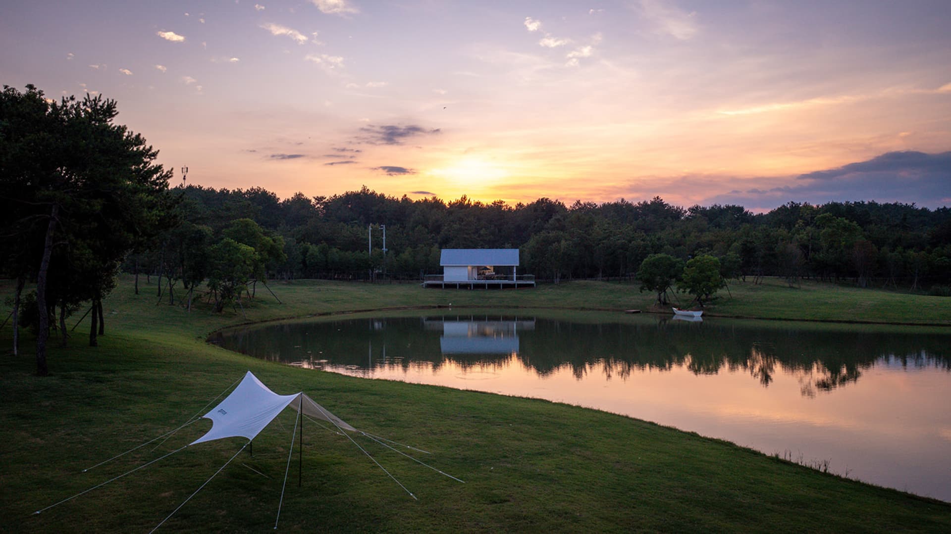 A house with a white exterior situated near a lake, surrounded by trees, with two boats and three people in the area
