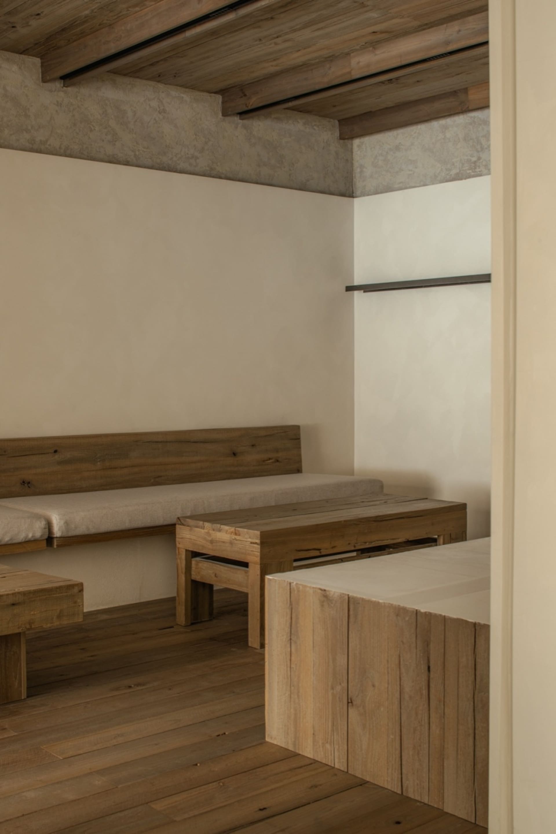 Small room with wooden floors, white walls, two beds with benches, and a dining table, creating a cozy and functional space