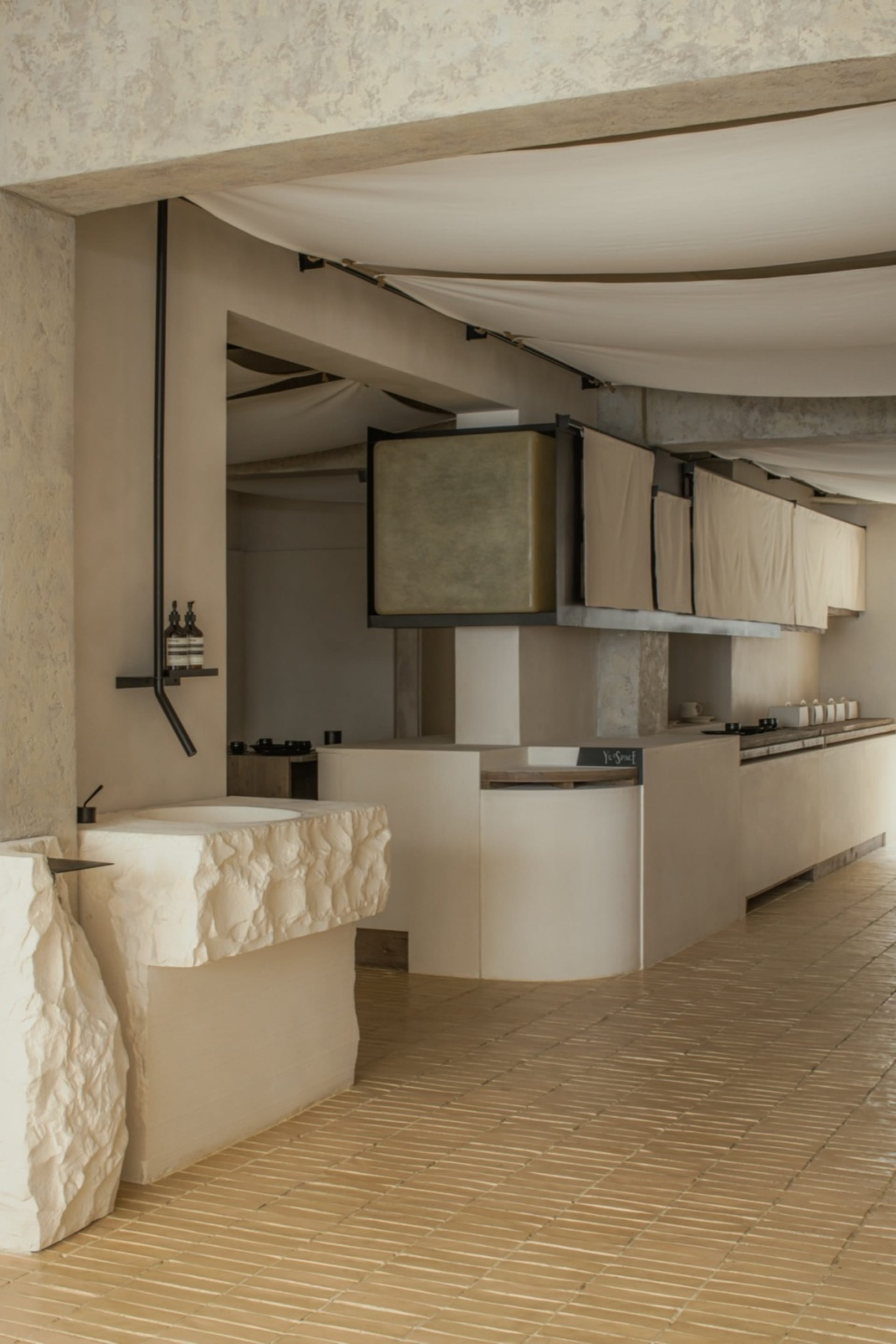 Empty kitchen space with white walls, brown tiled floors, two sinks, and dim lighting