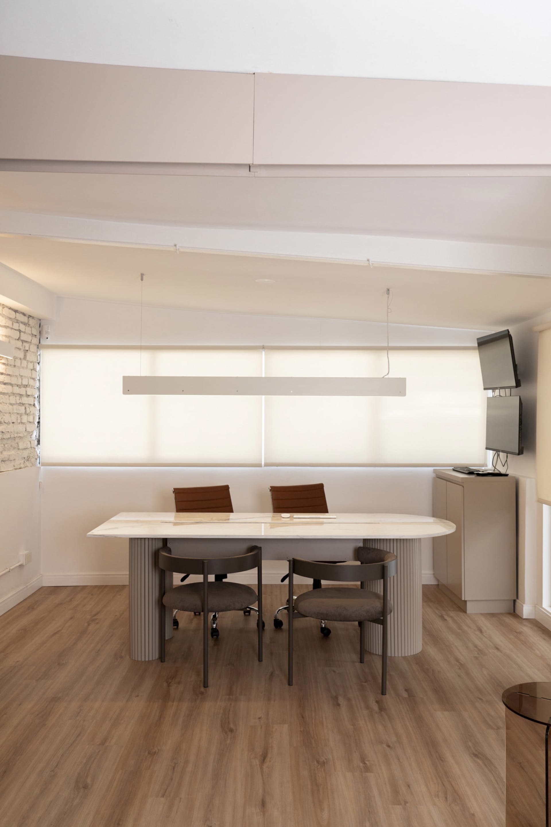 Professional office space with a large white desk surrounded by chairs and a mounted TV in a modern setting