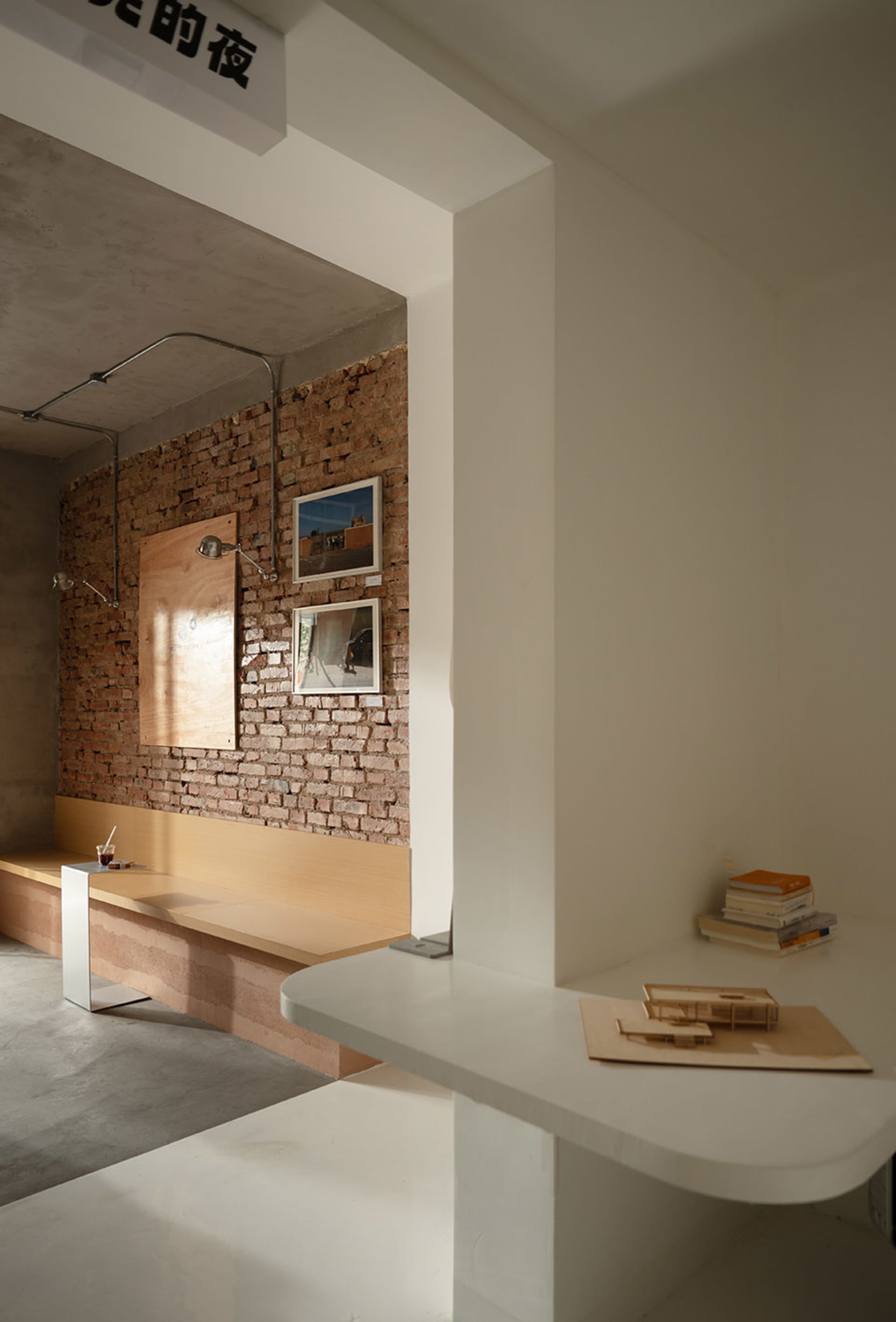 A room with a brick wall, a desk area, and a bench, featuring two pictures on the wall and a textured brick pattern