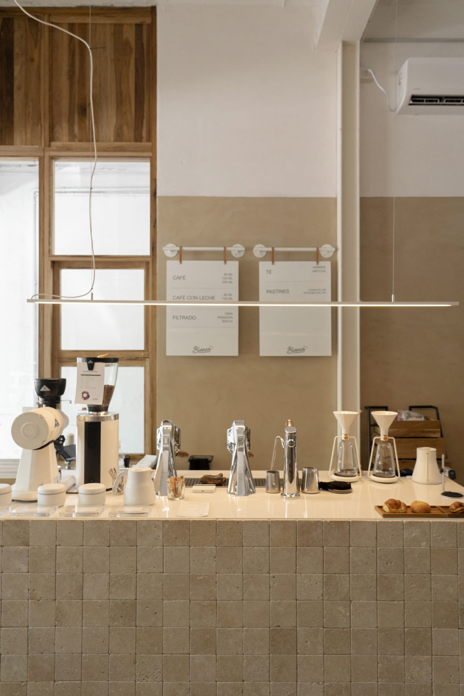 A cozy coffee shop interior with a counter, whiteboards, and various coffee machines and cups on display, surrounded by exposed brick walls and comfortable seating