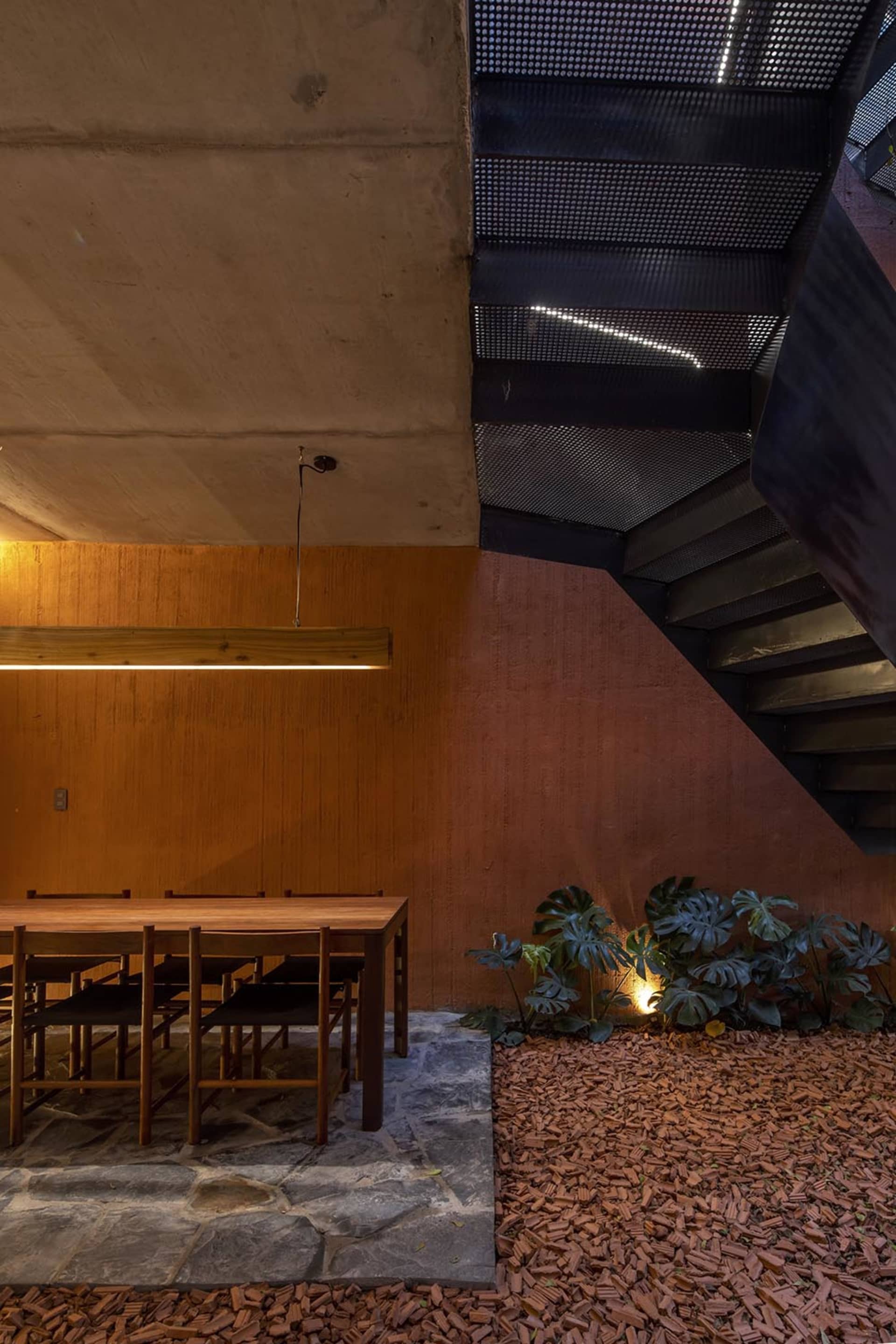 Modern staircase with concrete steps and metal railing, surrounded by a dining table and chairs in a well-lit space