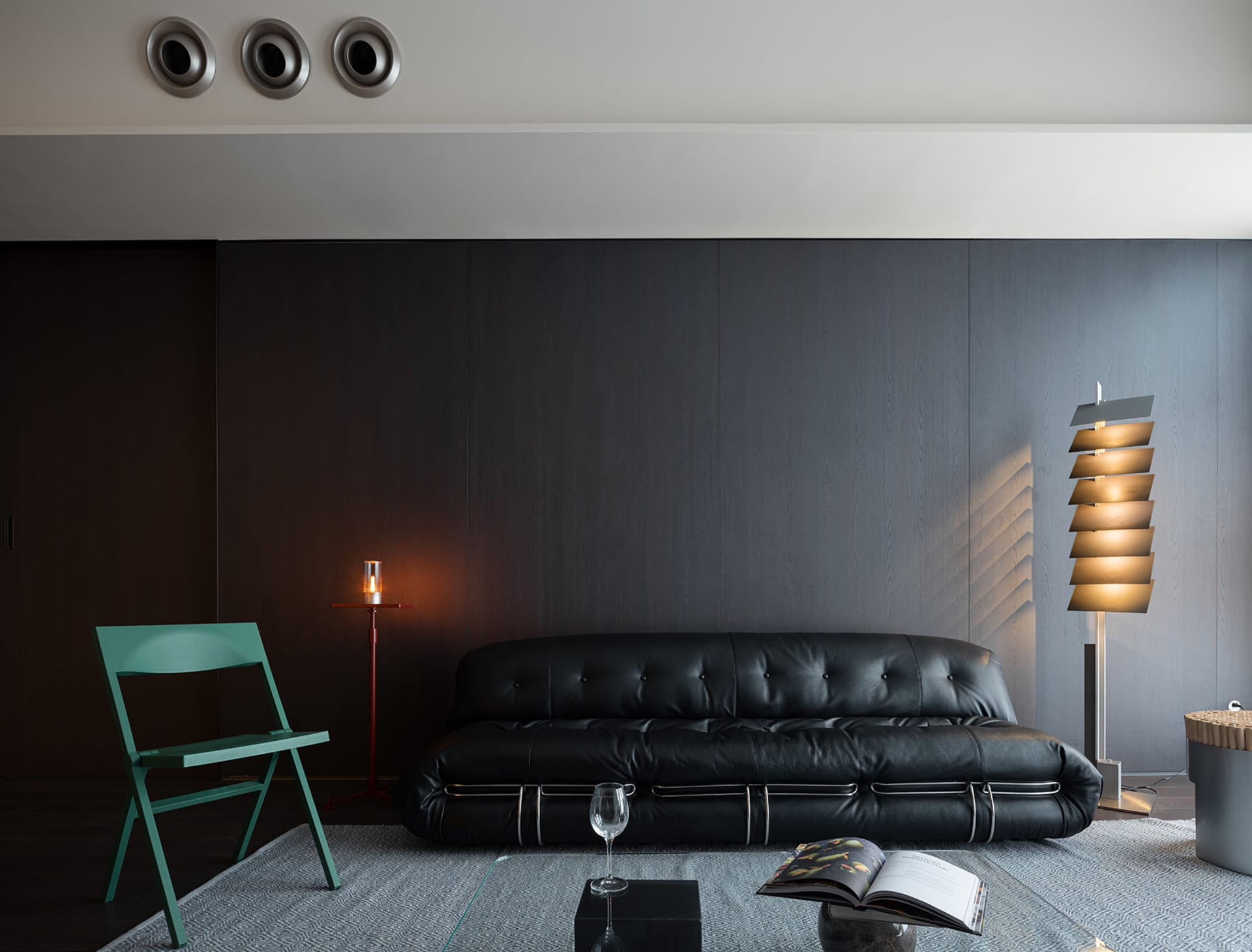 Cozy living space with a black leather couch, two chairs, and a wine glass, set against a wall