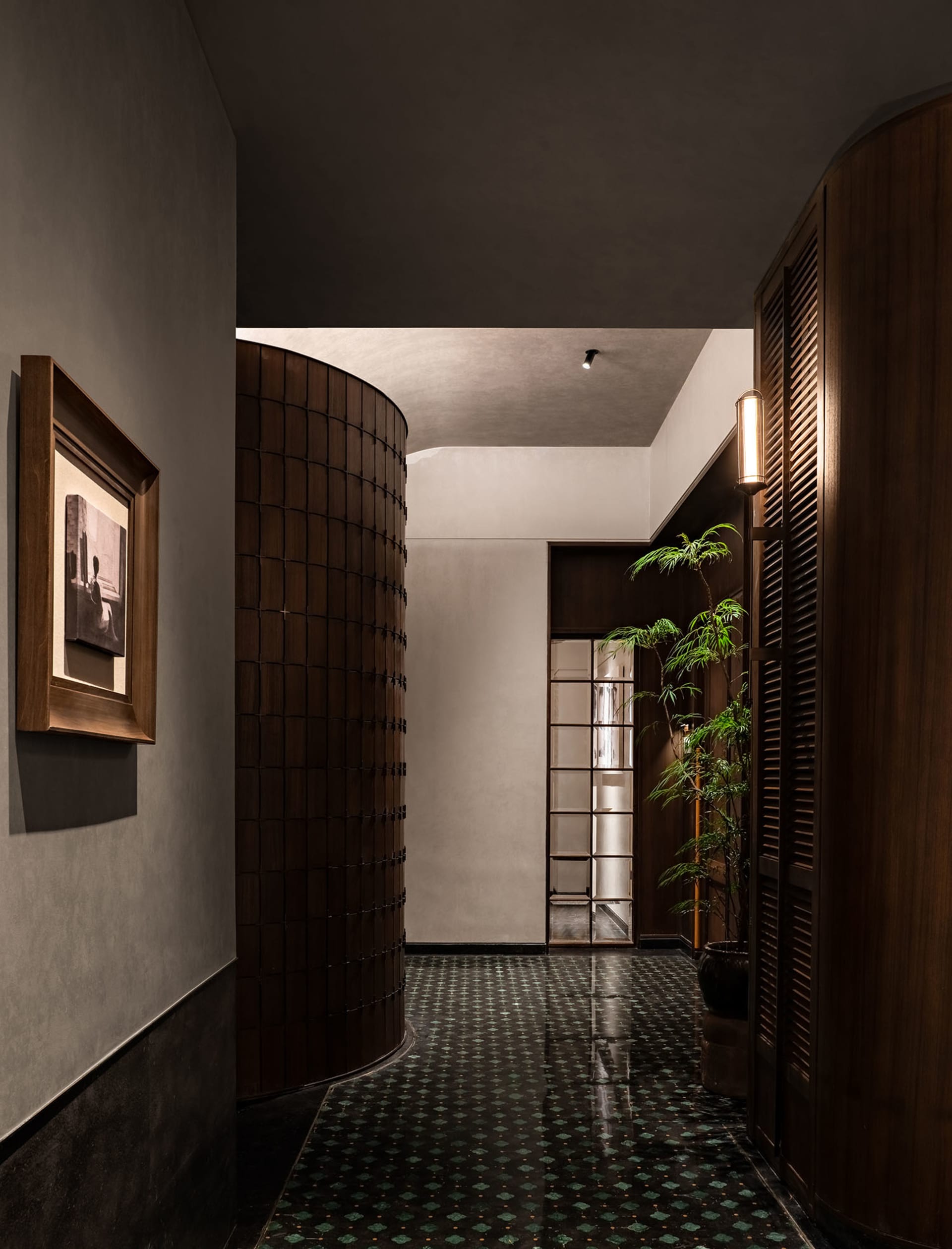 A calm and inviting hallway with a tile floor, wooden and glass doors, and two potted plants adding greenery to the space