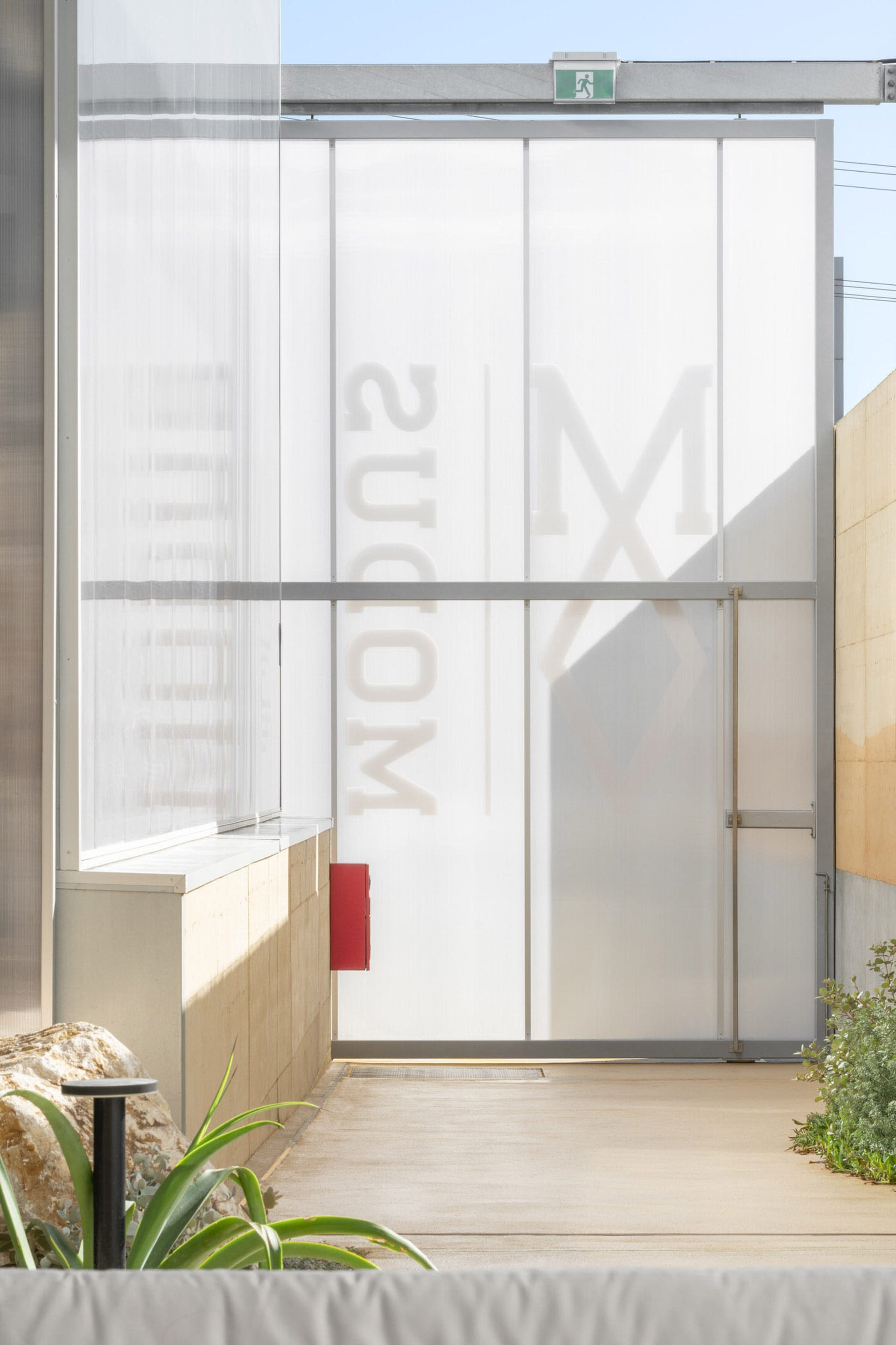 A modern building with a glass wall featuring letters and a metal facade with clear glass panels, set in a contemporary urban environment