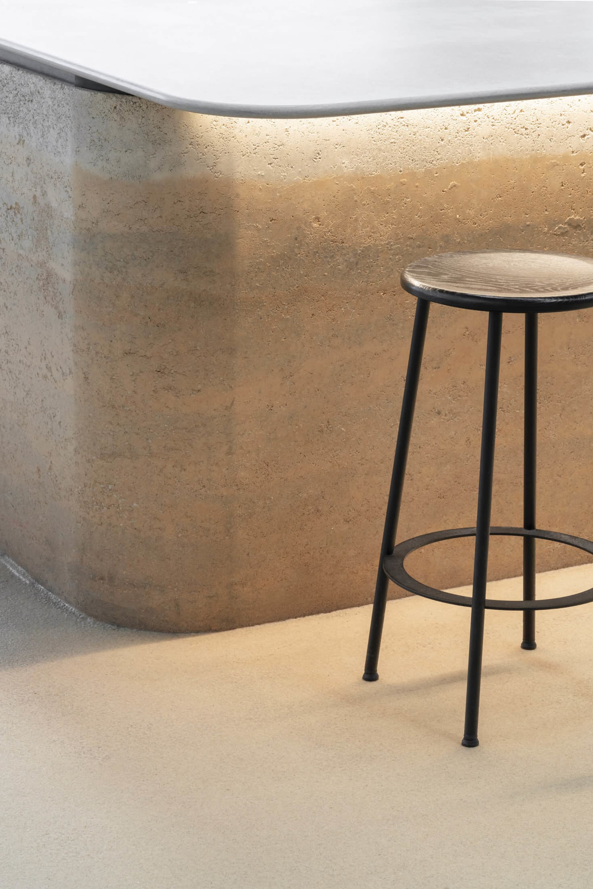 A minimalist space with a metal stool on a concrete floor, suggesting an industrial design style
