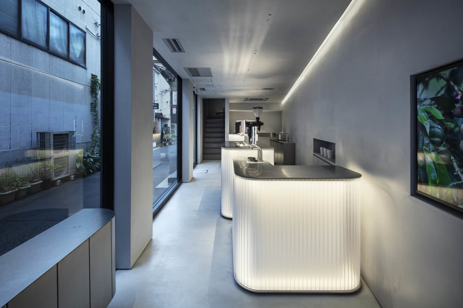 A modern restaurant interior with white walls and floors, featuring two large countertops, chairs, and a dining table, creating a clean and simple atmosphere