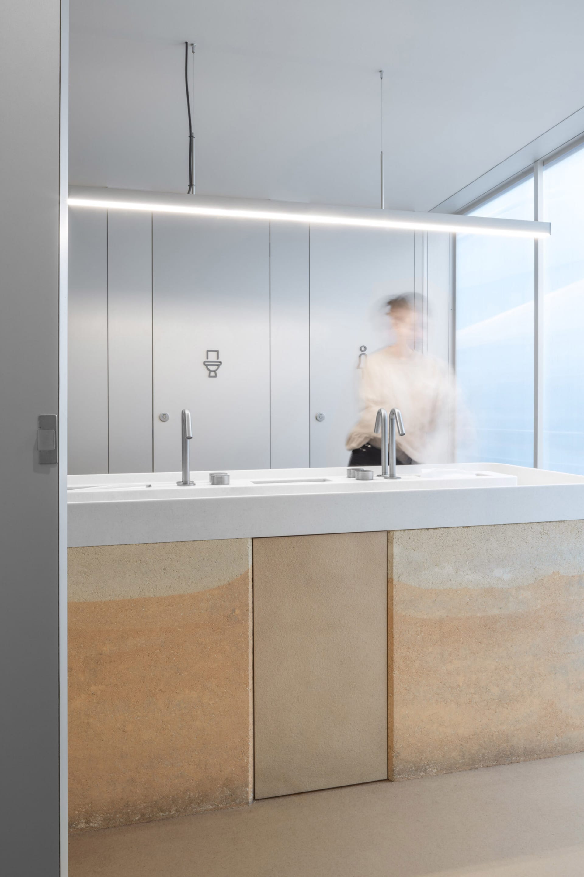 Modern bathroom with two sinks under a large window, two toilets, and ample space for users, with natural light entering the room