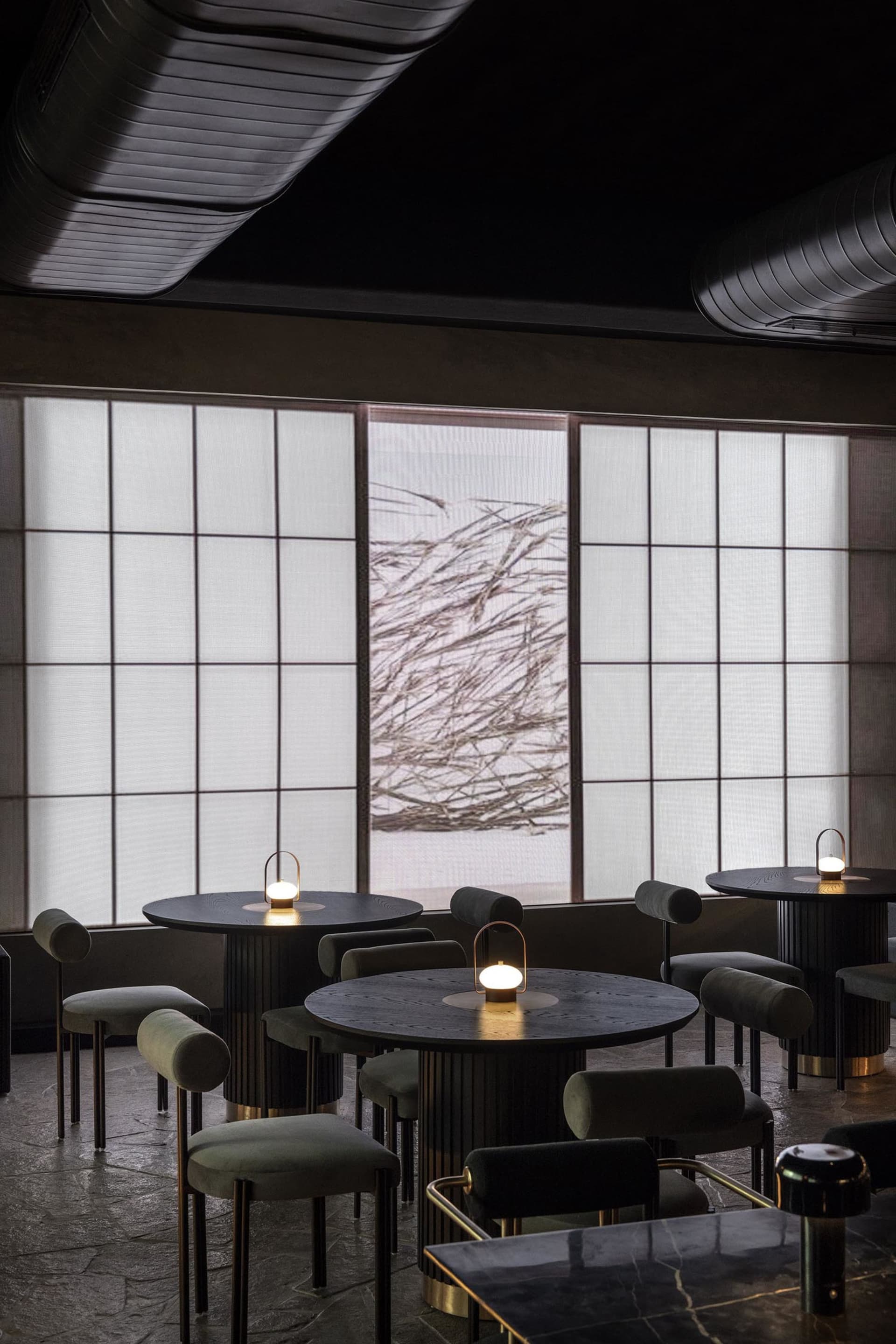 A restaurant interior with multiple round tables and chairs, lamps, and inviting atmosphere