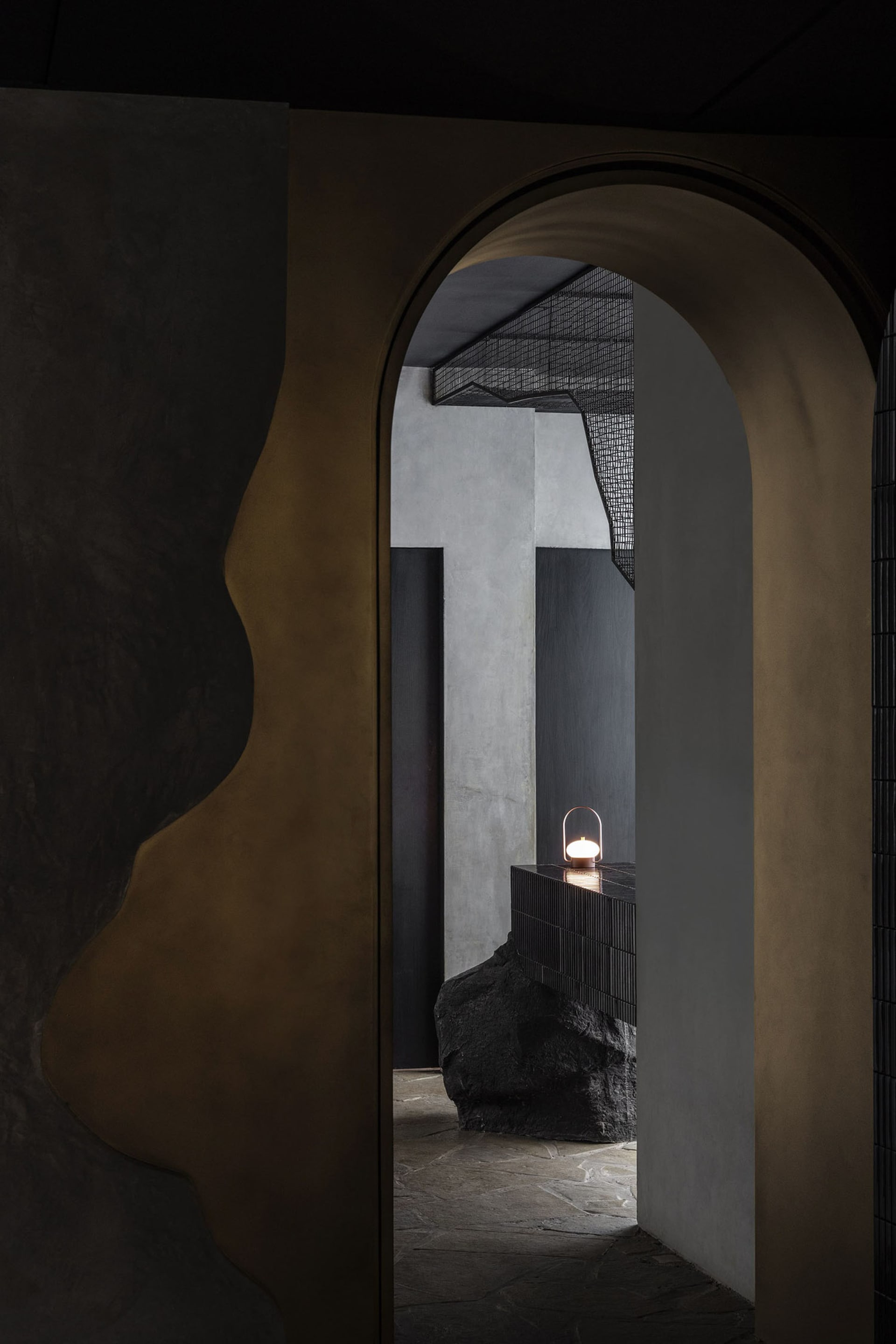Modern entrance with concrete walls, black pillars, and a gold-framed doorway, illuminated by a nearby light source