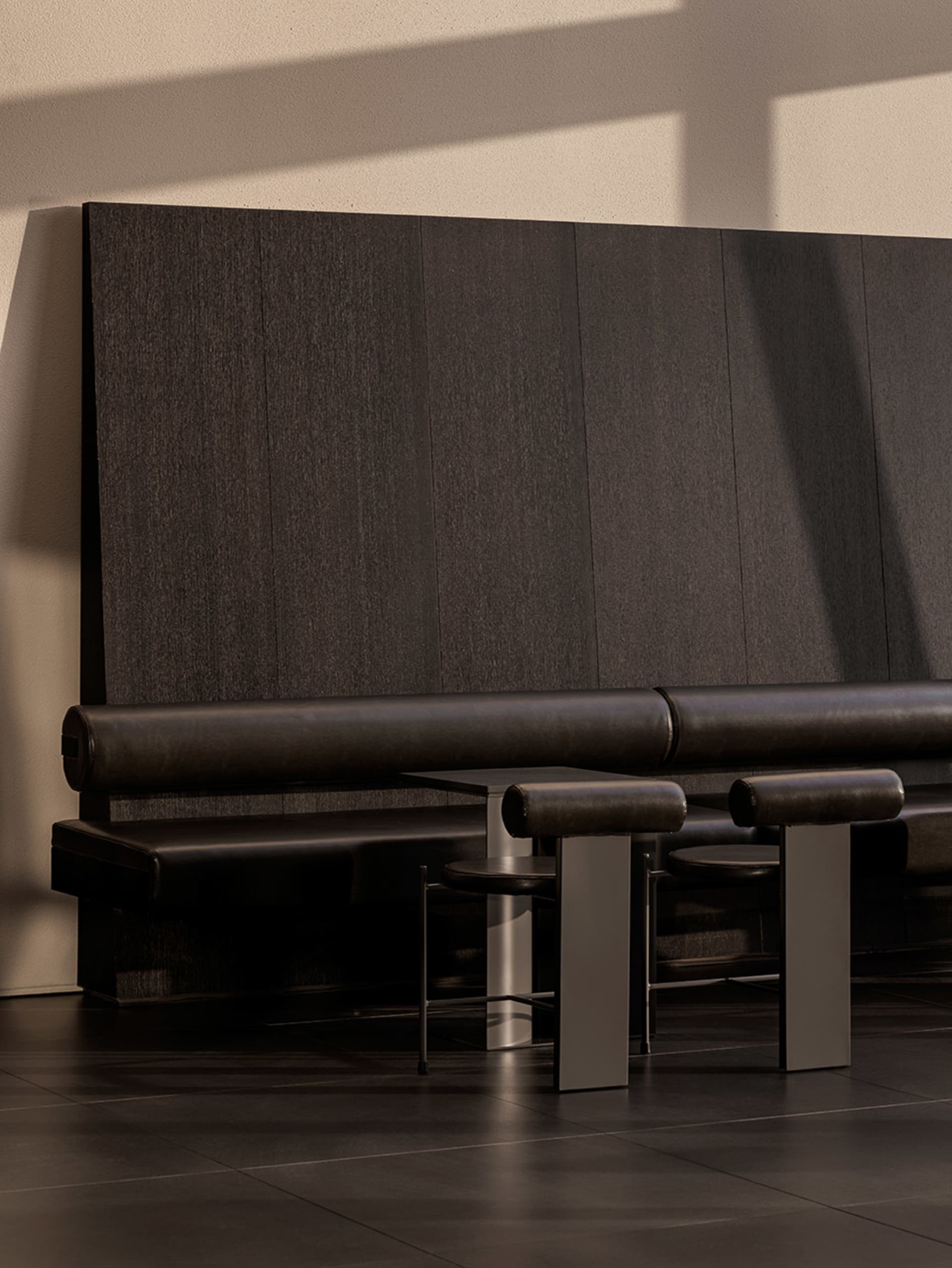 Empty room with a black leather bench and wooden wall, two chairs, and well-lit atmosphere