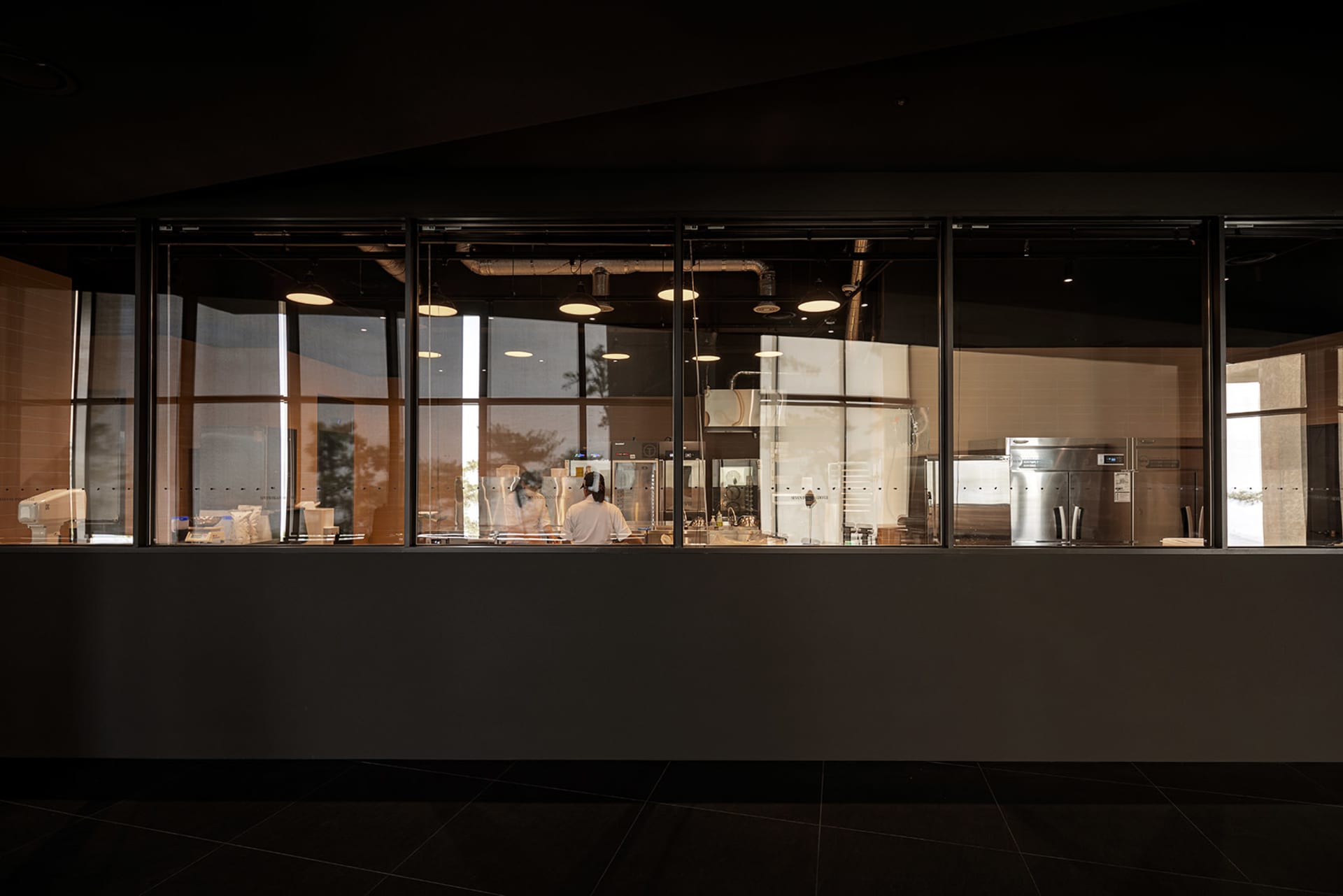 Industrial kitchen with two ovens, three refrigerators, and two people working, suggesting a busy and well-equipped commercial space