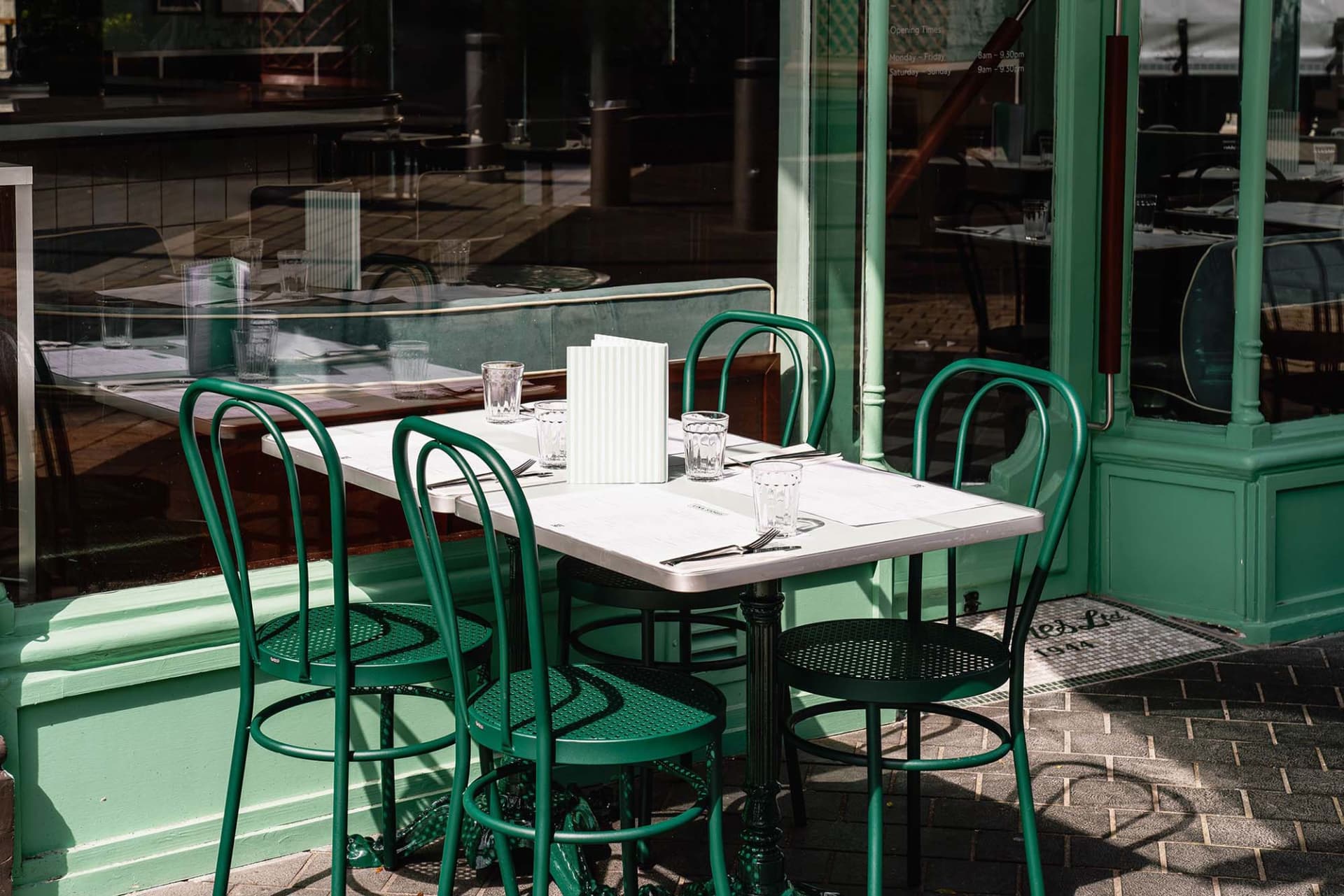 Outdoor dining area with a table surrounded by green chairs, cups, and a casual atmosphere