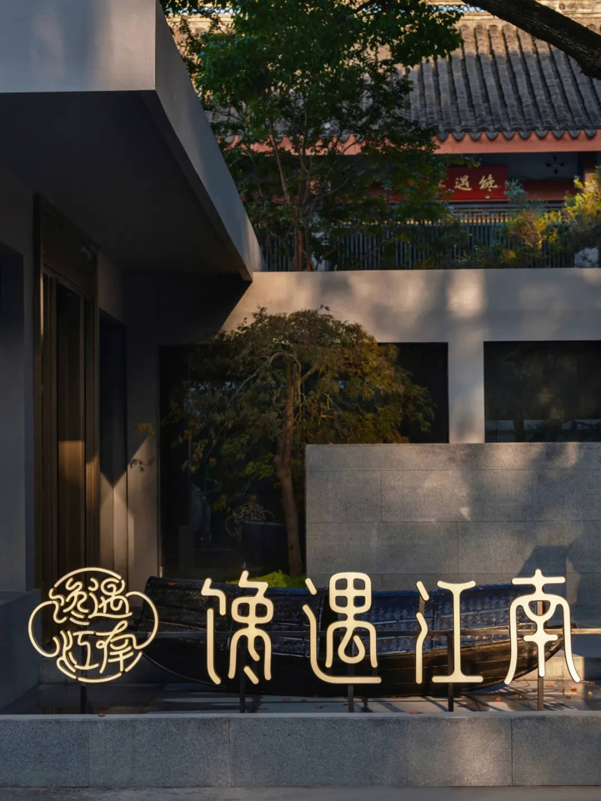 Asian-style house with a stone wall and a wooden boat in front of it, surrounded by trees, with a modern and traditional feel