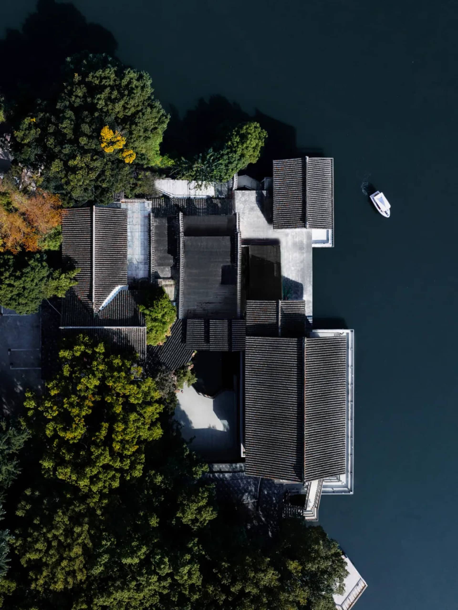 水邊亞洲風格住宅，配有黑色屋頂，周圍環繞樹木，附近停靠一艘小船