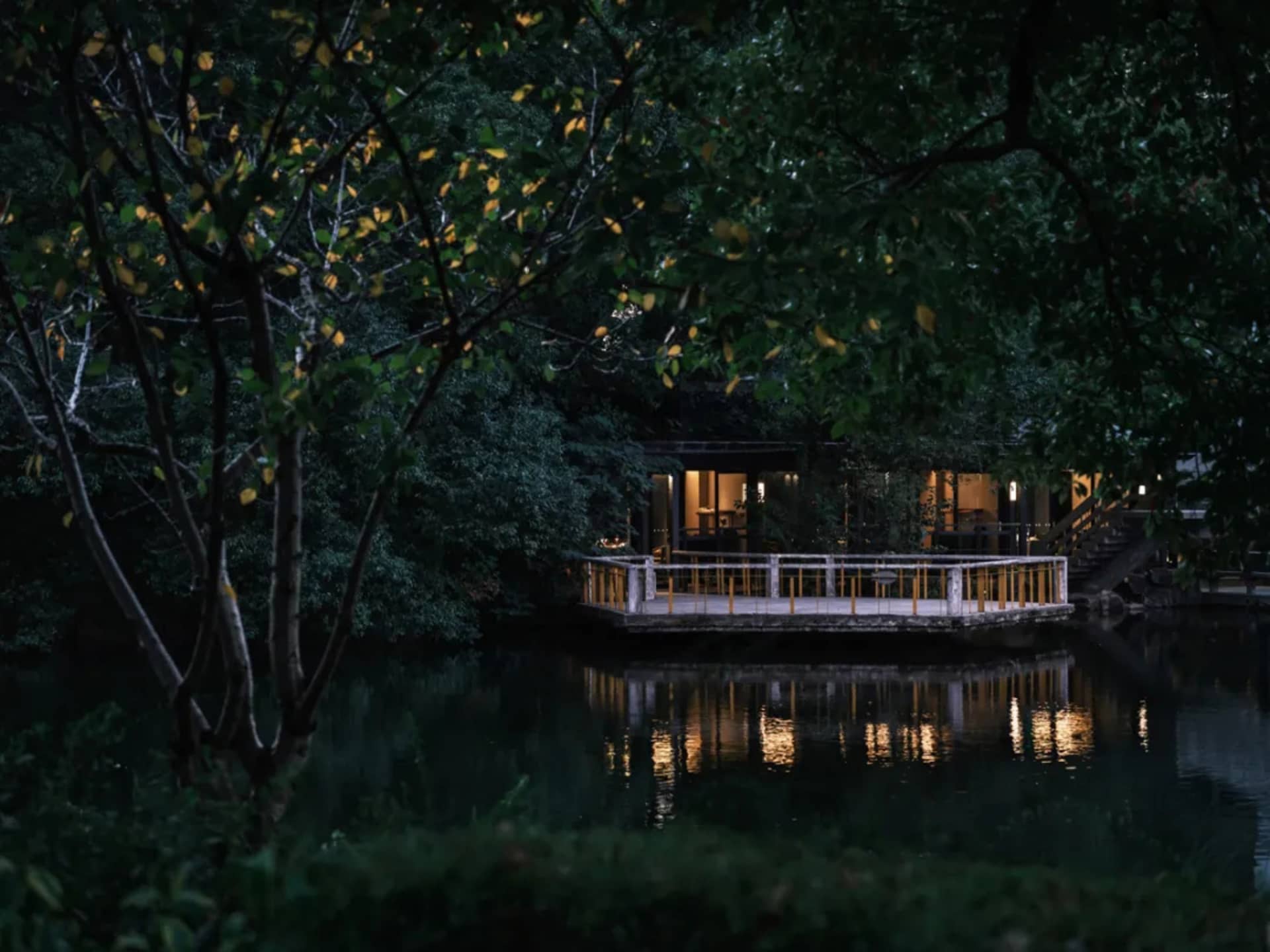 A serene Asian-style house near water with a wooden structure, yellow accents, and a balcony overlooking the water