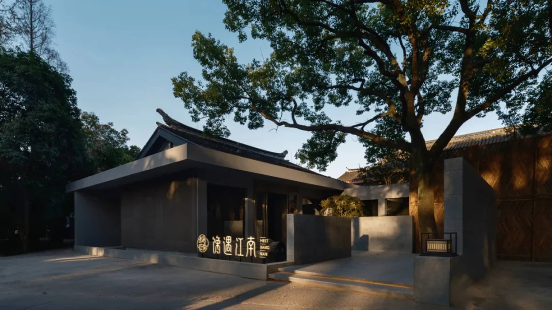 灰色混凝土外牆的亞洲風格建築，周圍環繞兩棵樹木與自然植栽