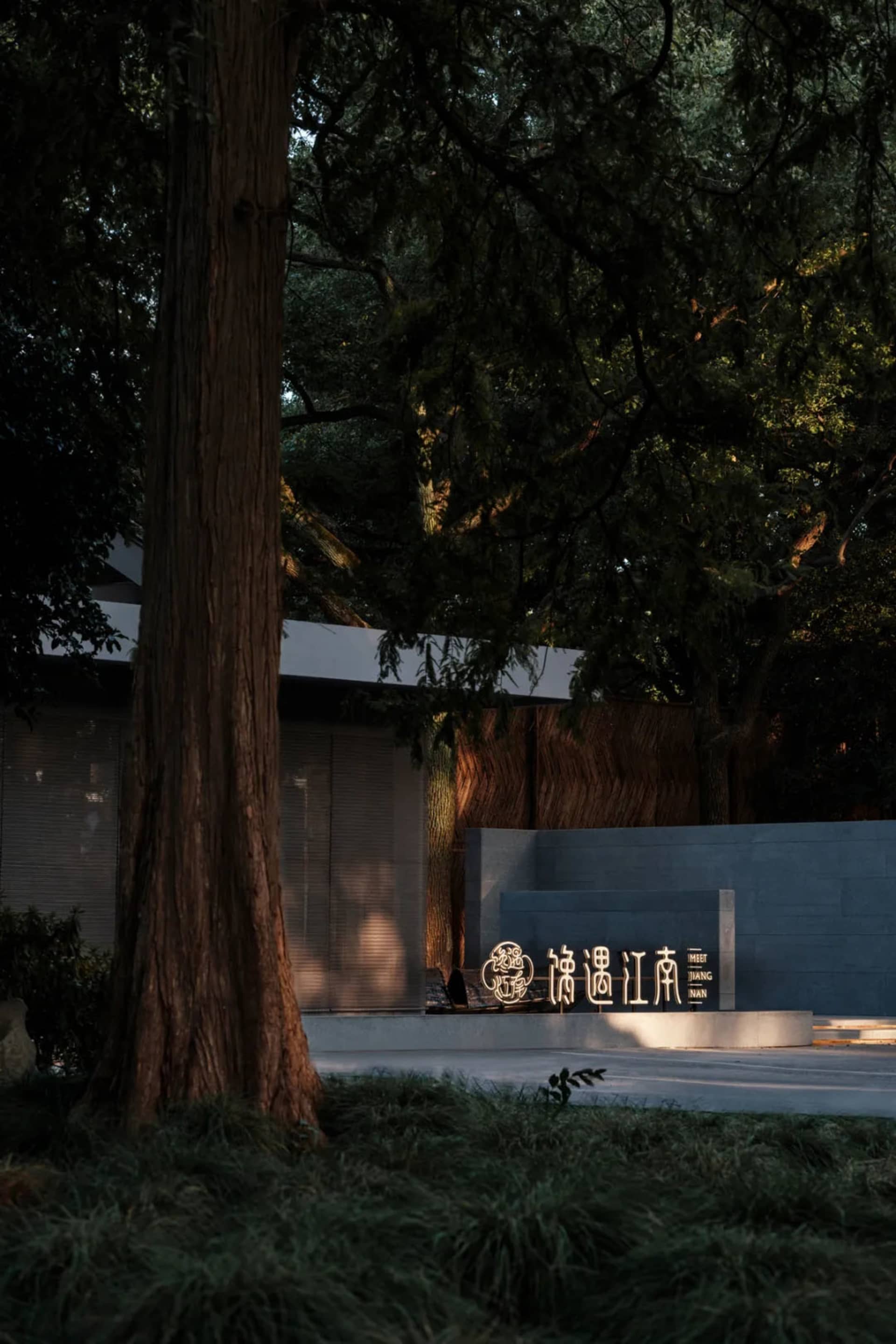A serene Asian-style building with a stone wall and a large tree in front, featuring a modern concrete structure with a gray appearance