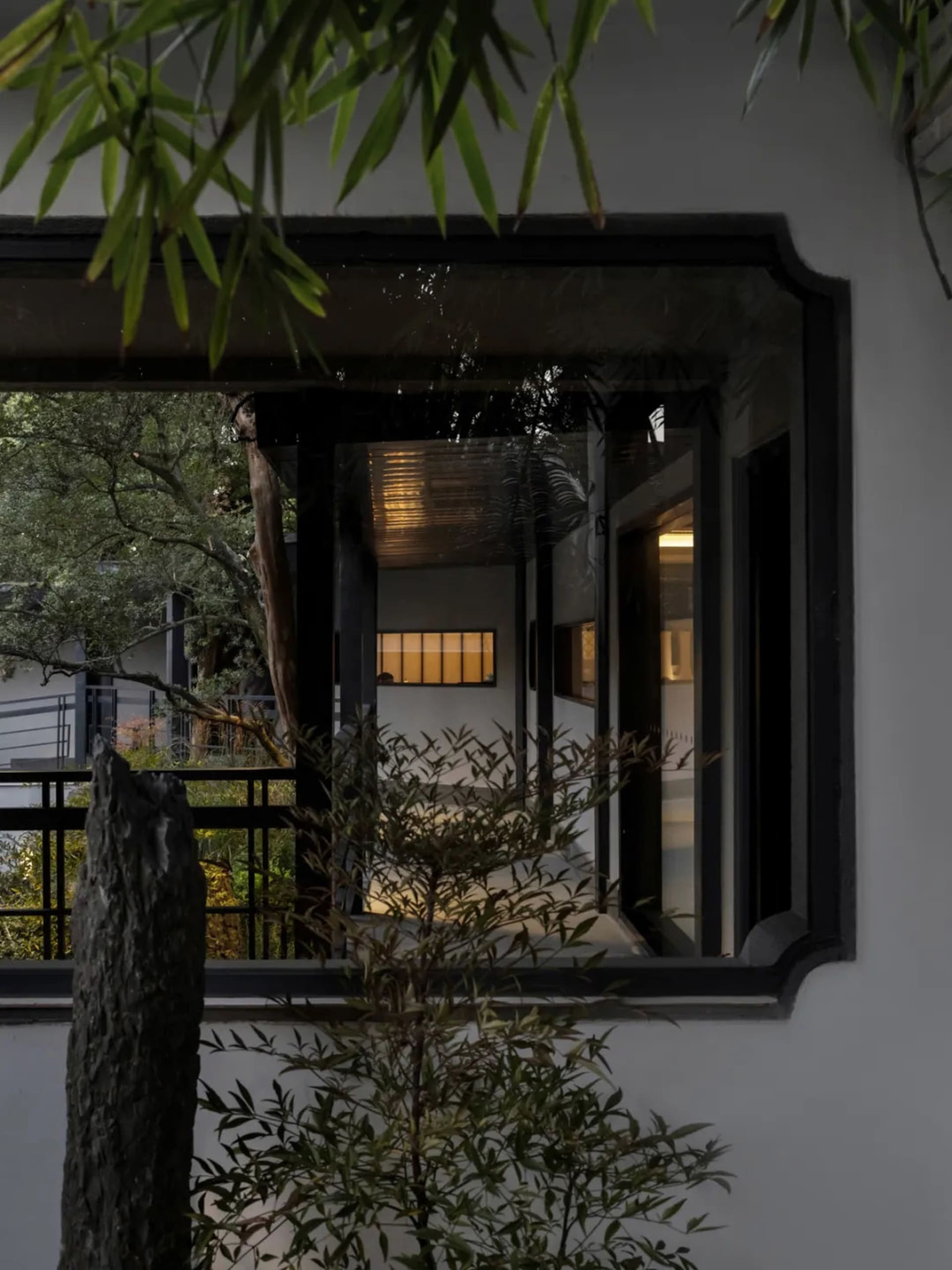 Asian-style house with a large window, black door, white wall, potted plants, and a bench in a well-lit room