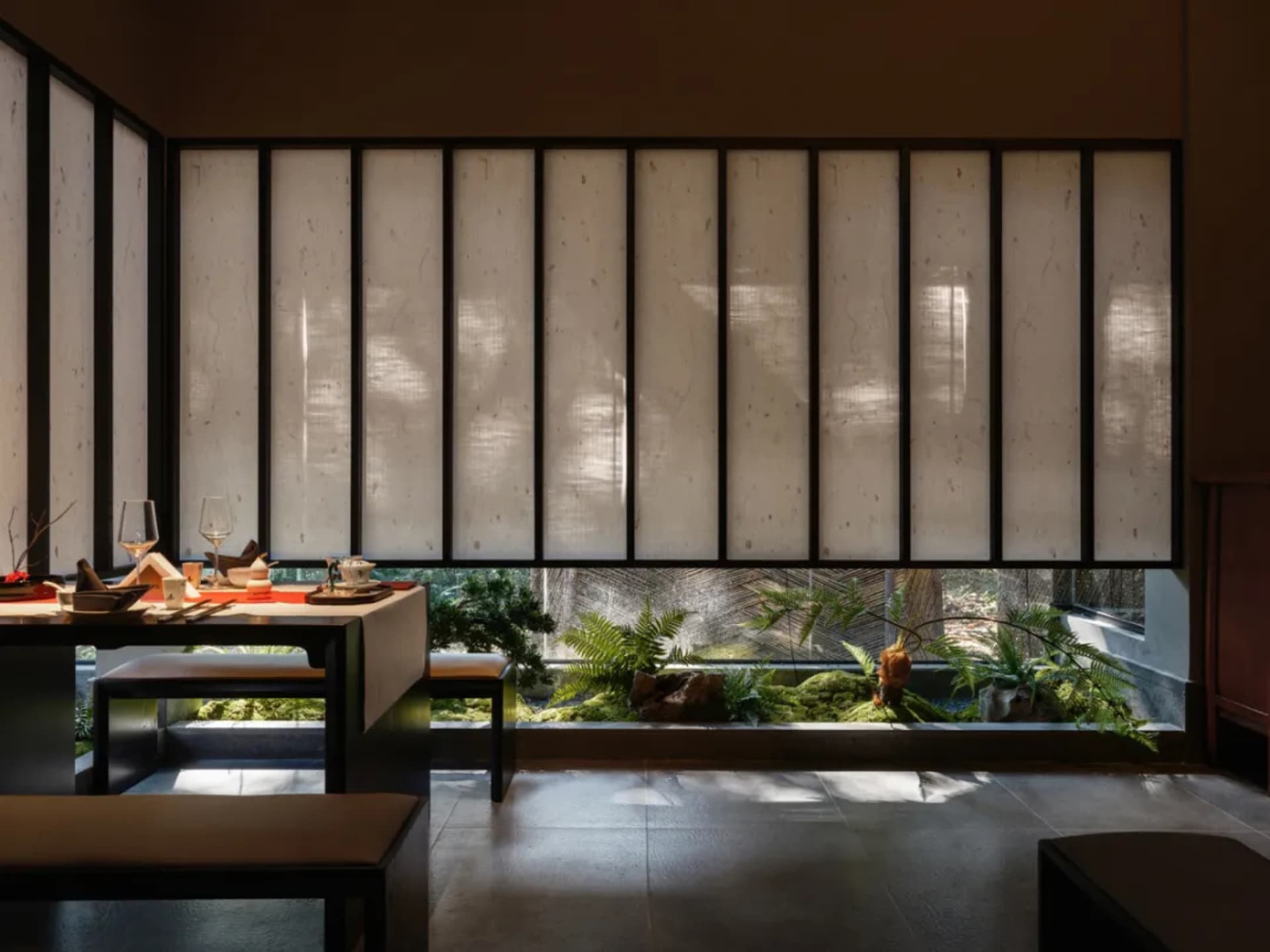 Bright dining space with two tables, chairs, and wine glasses, surrounded by a modern interior with a large window for natural light
