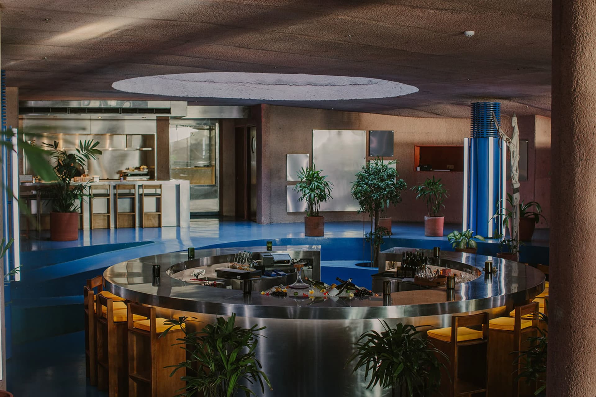 A modern restaurant with a circular dining table, potted plants, and brown walls creating a warm atmosphere