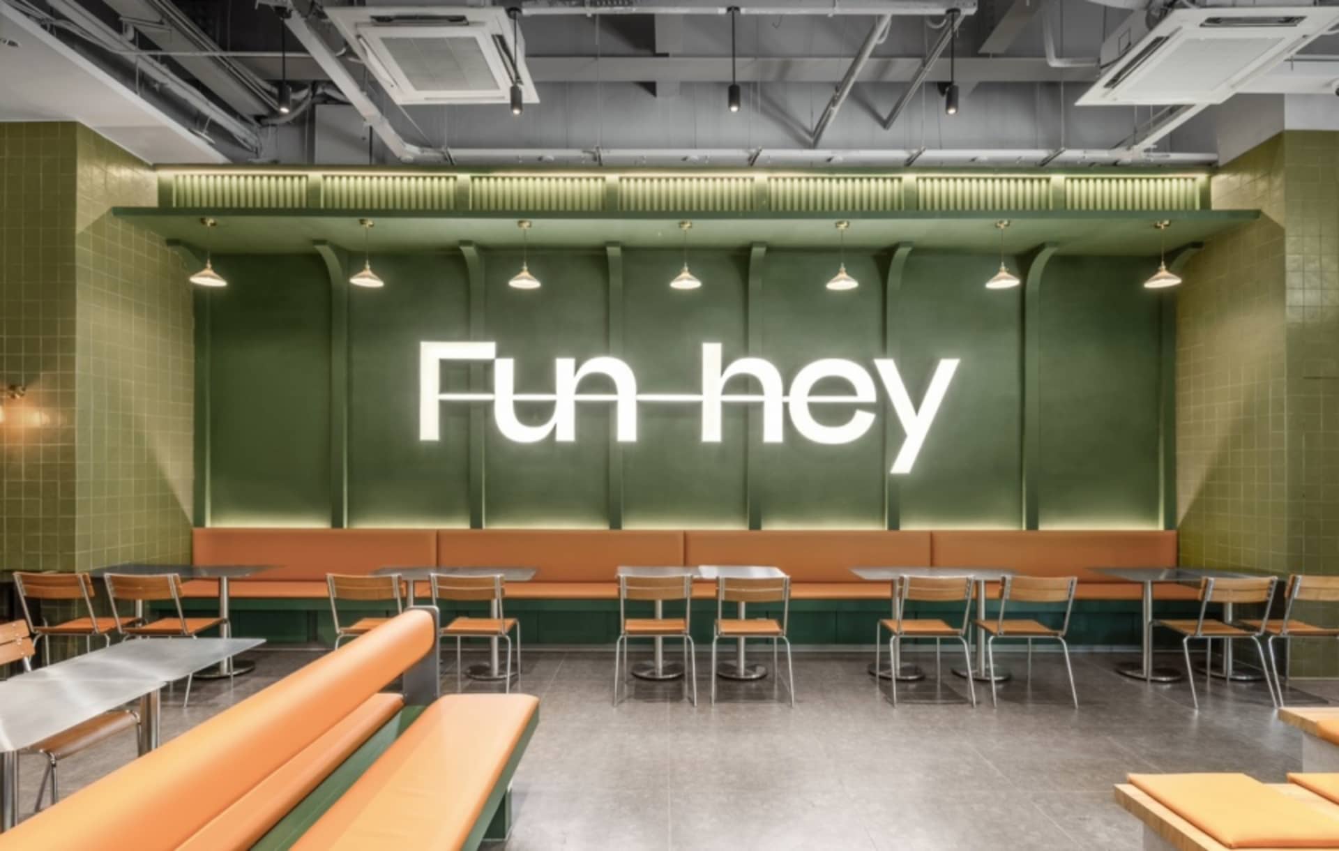 A modern restaurant with a green wall, dining tables, and benches, creating a casual atmosphere for guests
