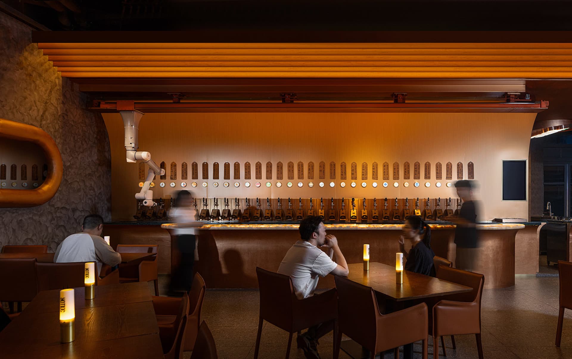 Cozy bar area with a long wooden counter, chairs, and dining tables, featuring multiple beer taps and candles