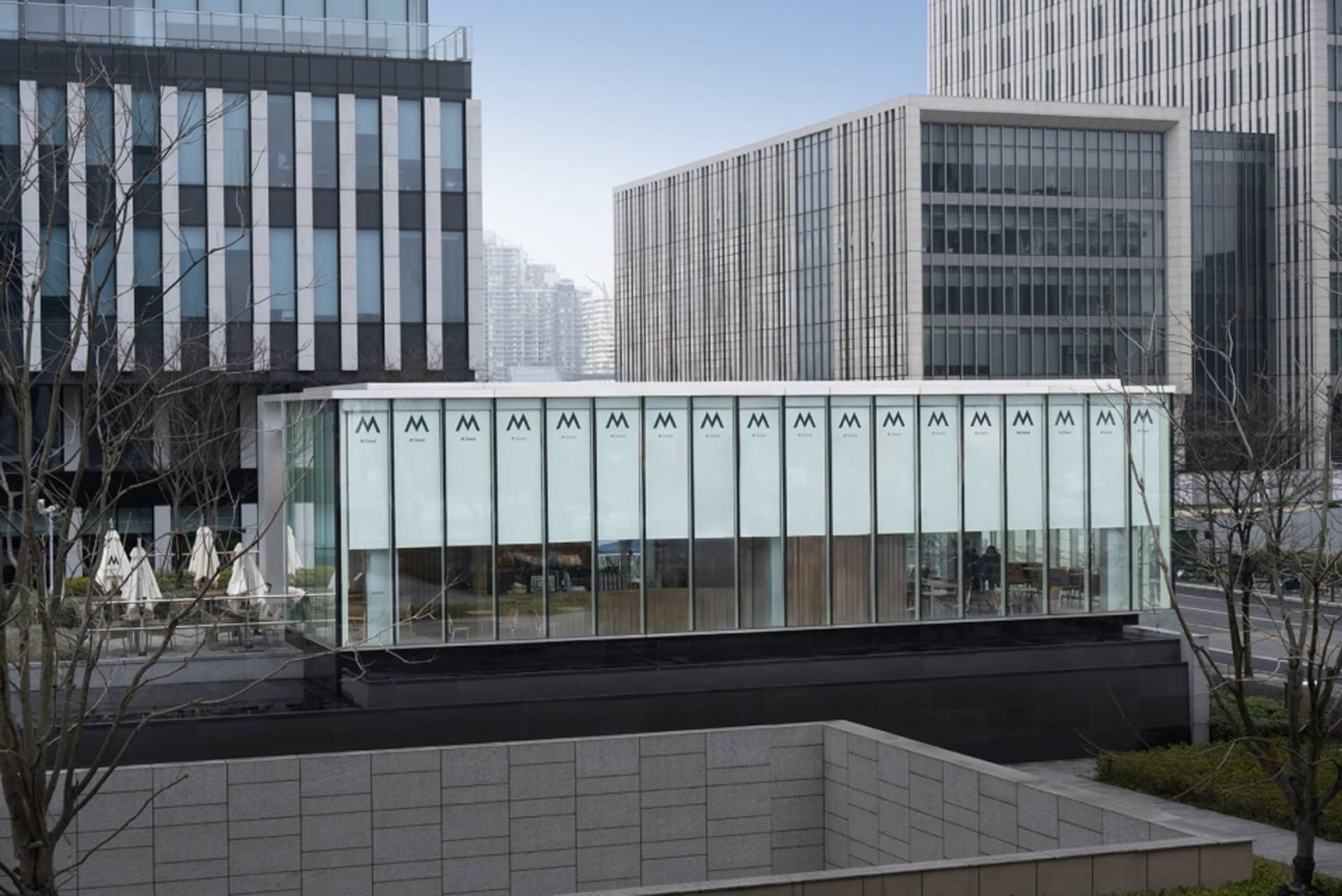 現代建築擁有玻璃外牆、白色牆面與黑色屋頂，位於當代都市環境中，人們站在窗戶附近