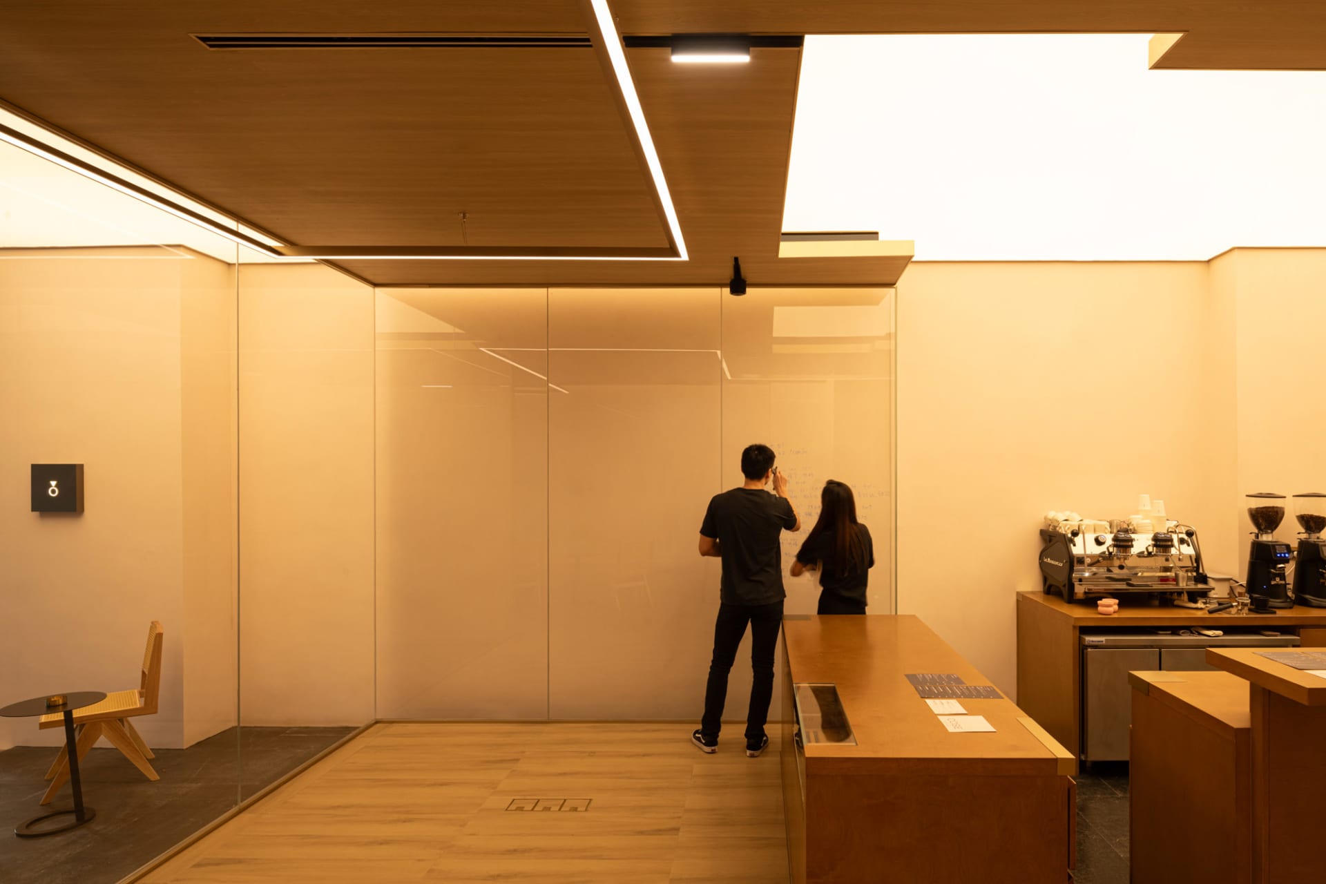 Two people in a modern office with a glass partition, wooden floor, and countertop, creating a warm and professional atmosphere