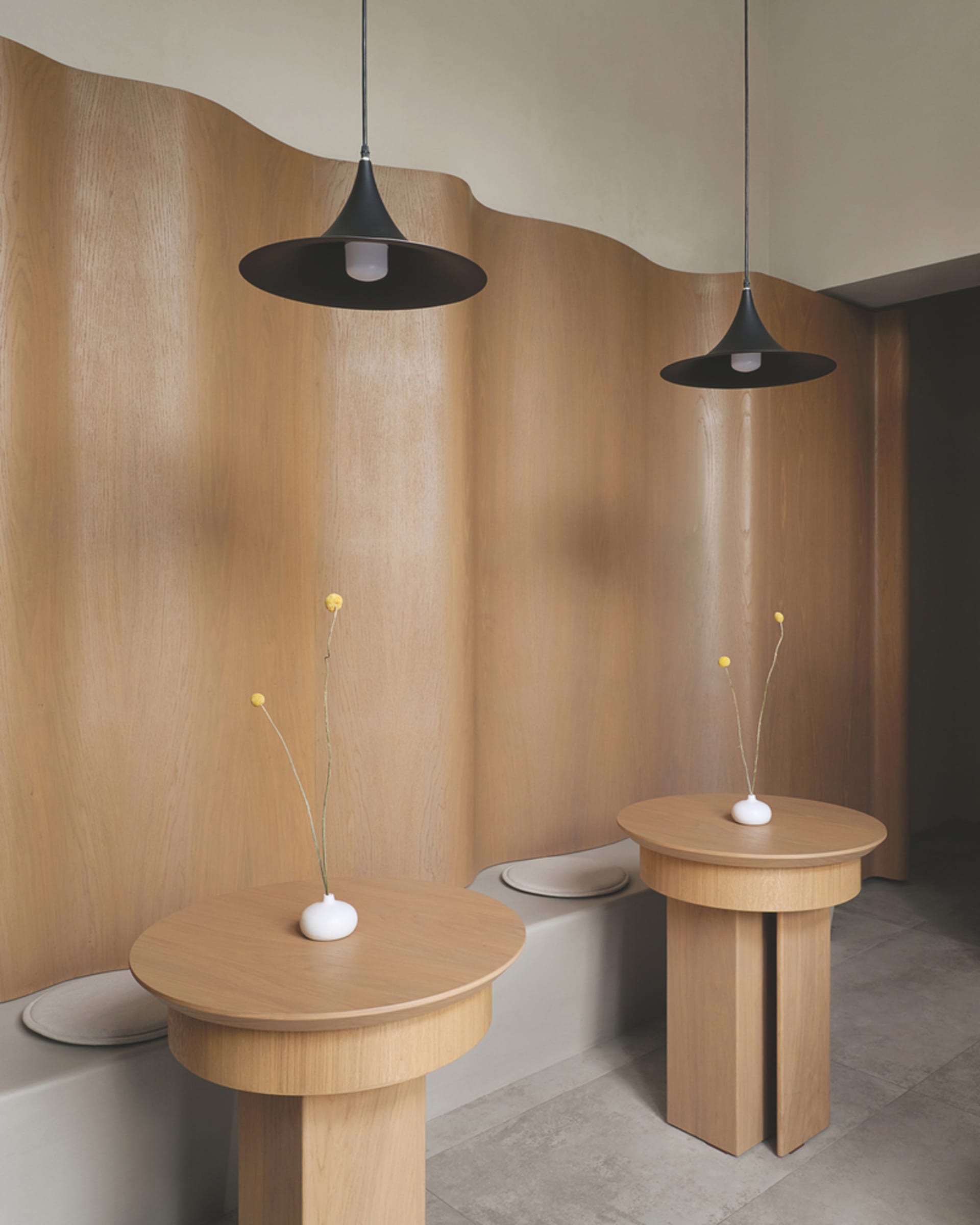 A cozy room with two wooden tables, vases, and potted plants, surrounded by wooden walls, creating a warm and inviting atmosphere