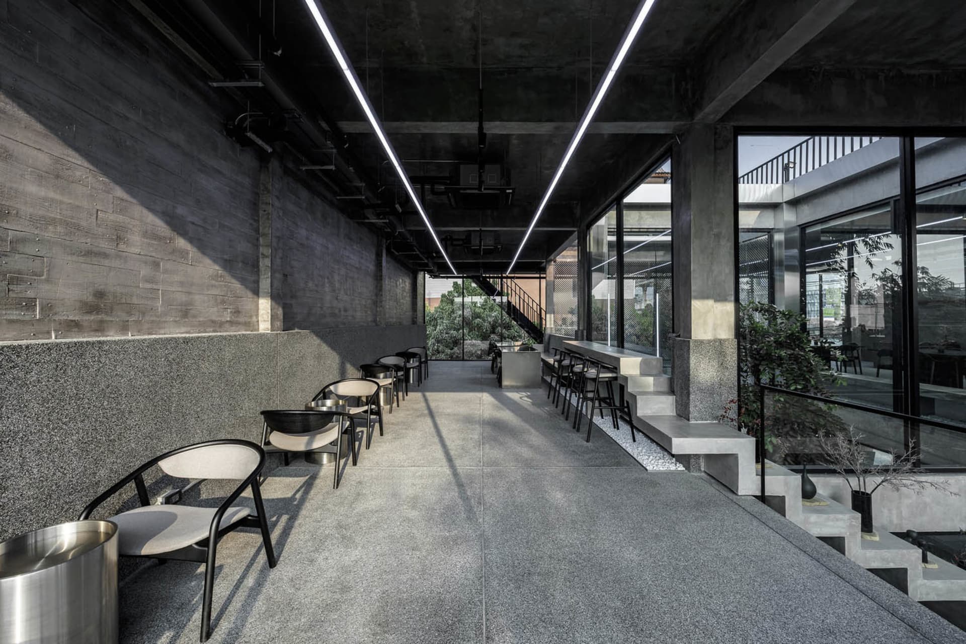 Spacious modern lobby with concrete floors and walls, featuring seating areas with chairs and dining tables, and an inviting atmosphere